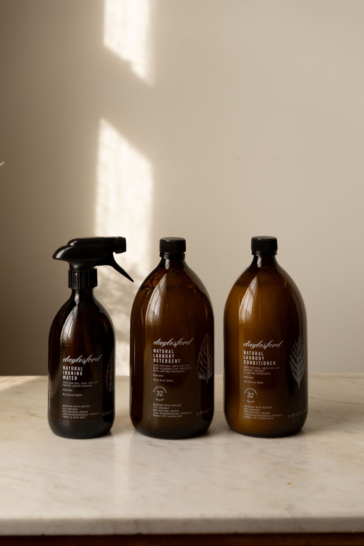 Three Daylesford natural cleaning products in amber glass bottles arranged on a white marble surface in warm light.