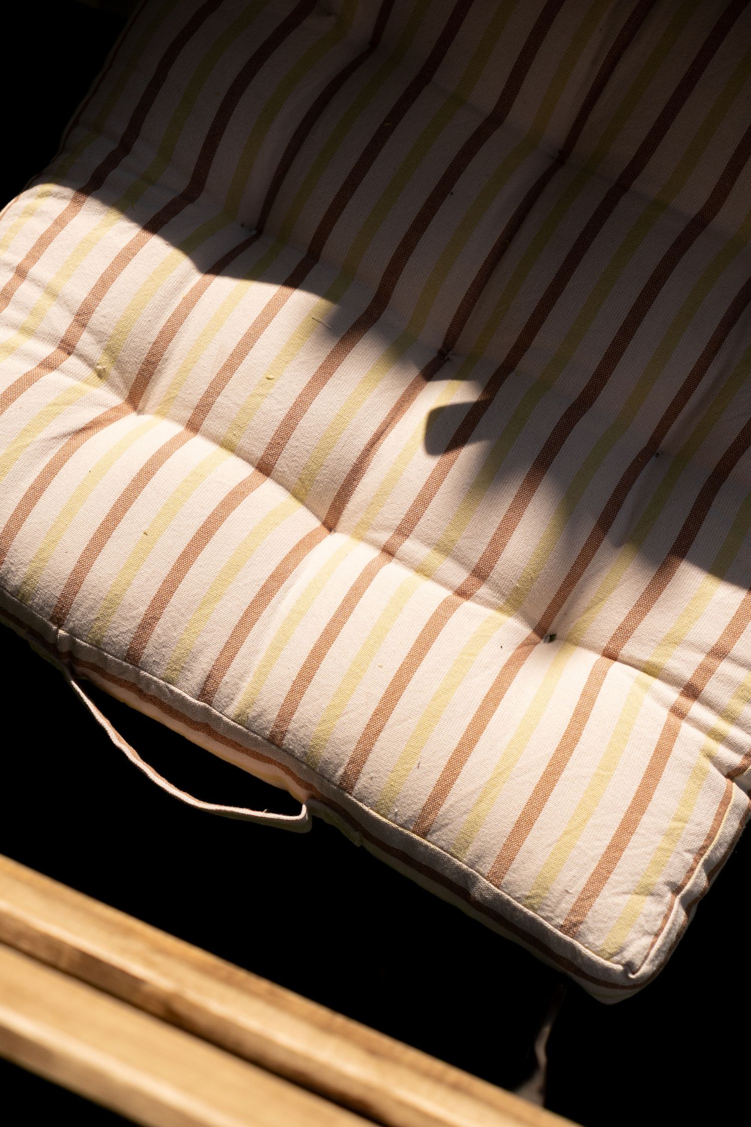 Striped cushion pad on a wooden chair casting shadows in warm sunlight.
