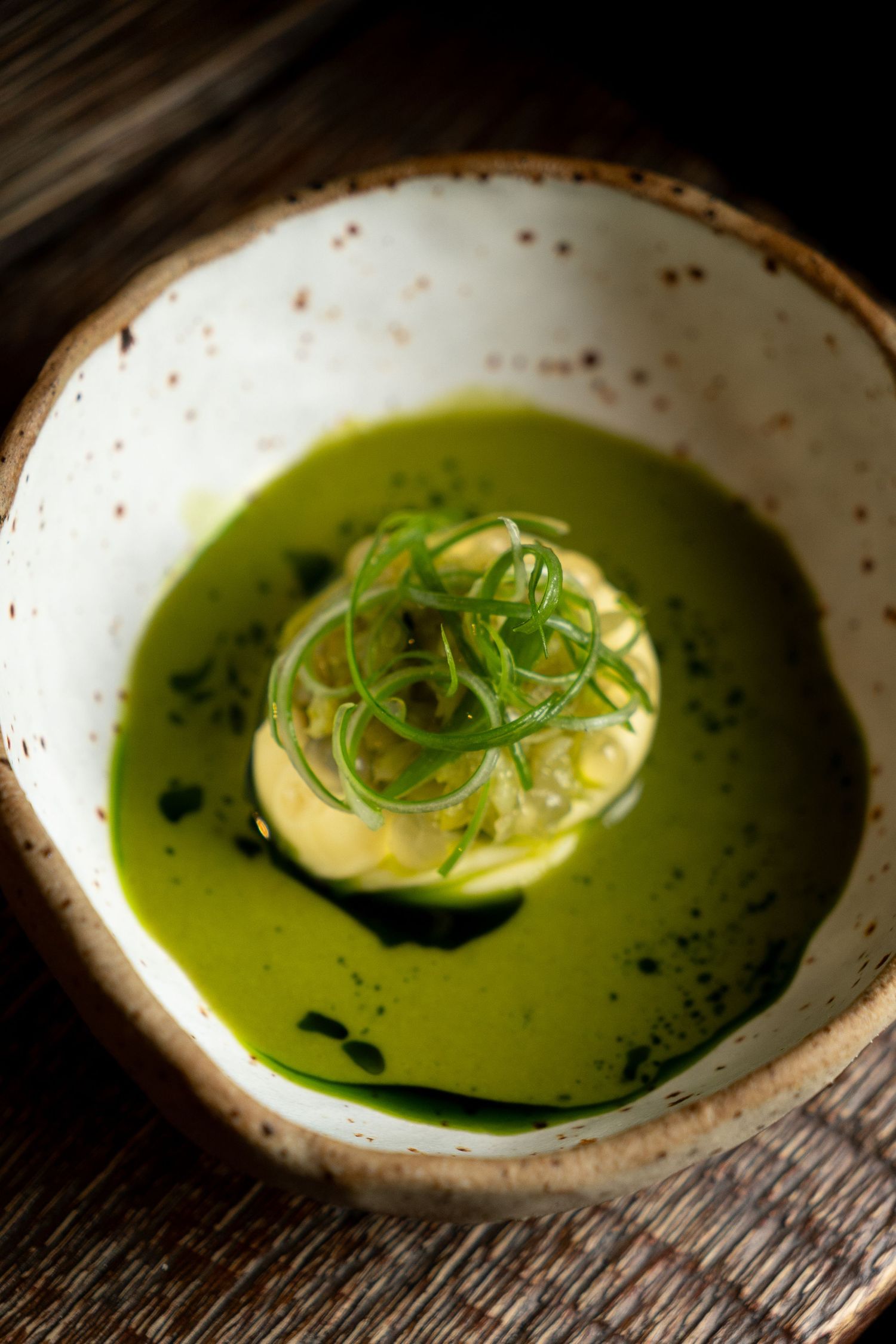 Vibrant green herb soup with cream garnish served in a speckled ceramic bowl.