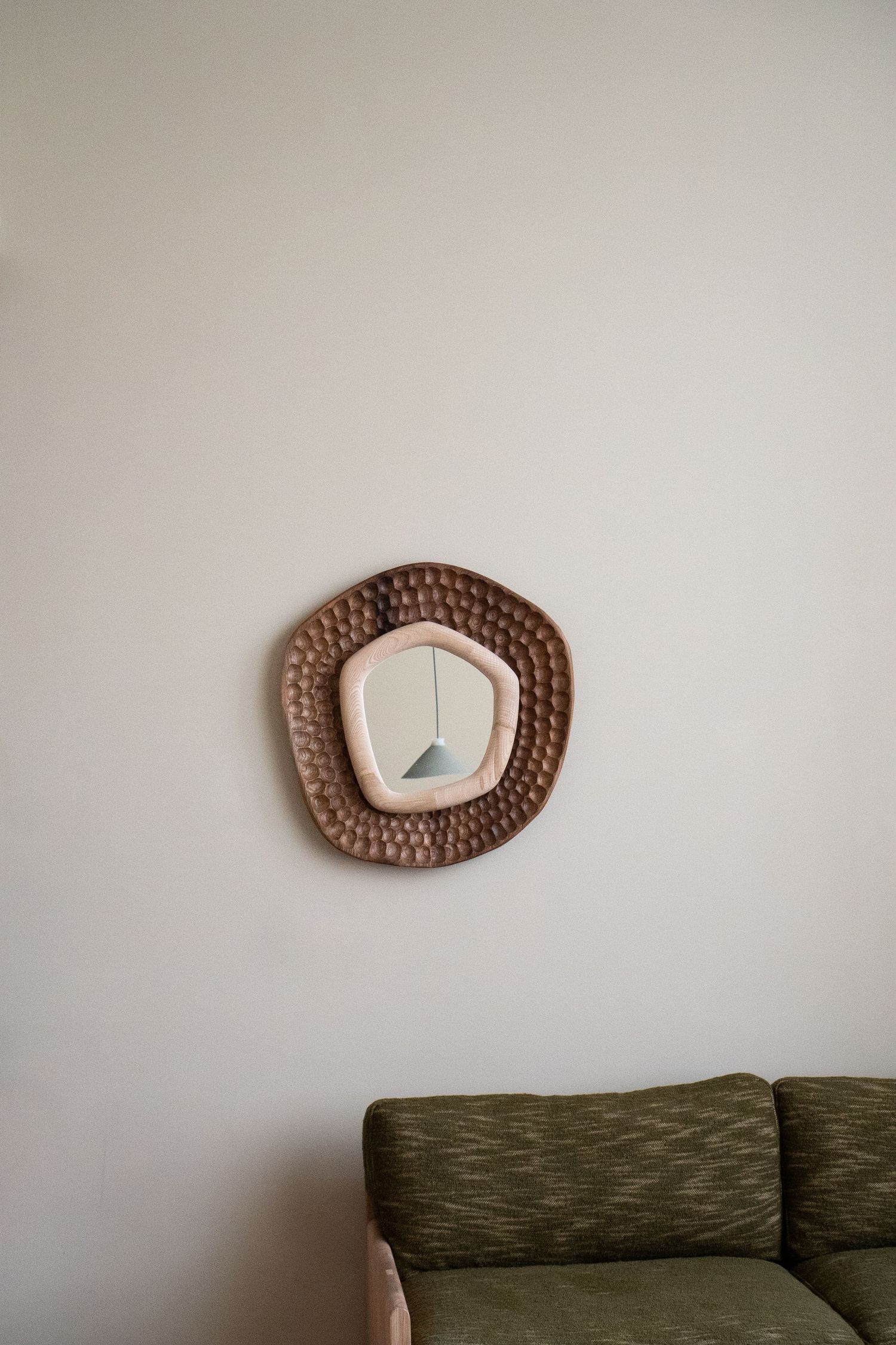 Rustic woven rattan mirror with organic shape hanging on white wall above green textured sofa.