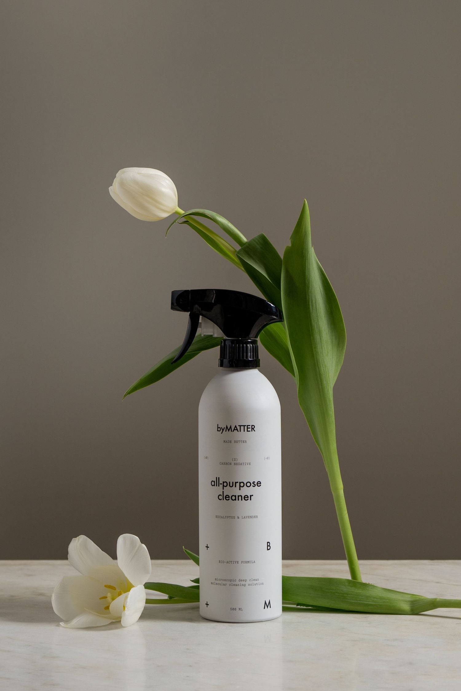 byMatter all-purpose cleaner spray bottle in white with black nozzle displayed with fresh white tulips on marble surface.