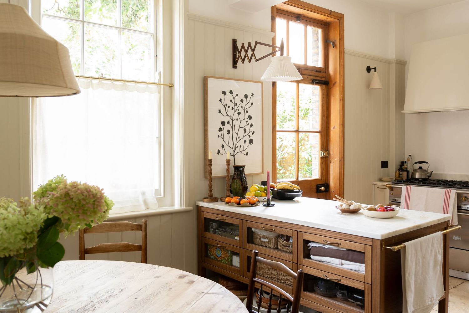 Warm kitchen interior with wooden island, marble countertop, large windows, and fresh hydrangea flowers.