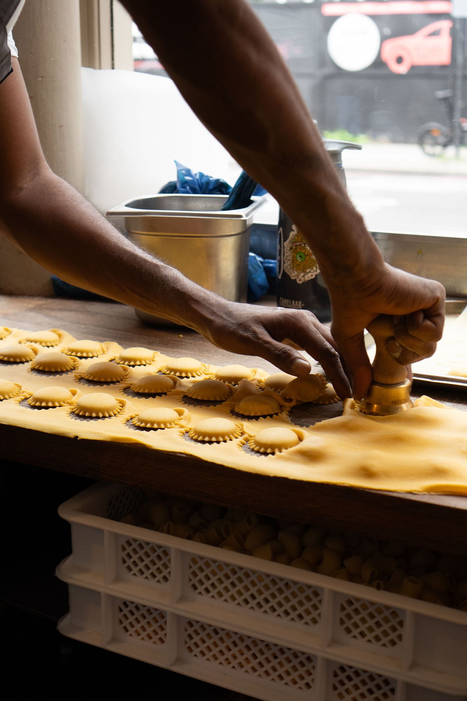 Chef hands cutting fresh ravioli pasta dough with round cutter tool on wooden kitchen counter.