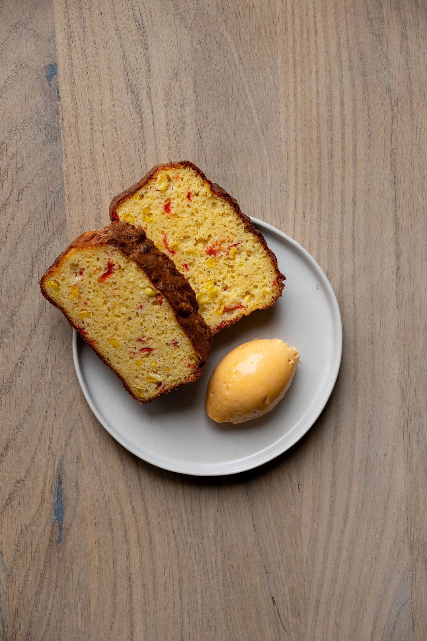 Two slices of red pepper corn bread served on a white plate with a scoop of butter.