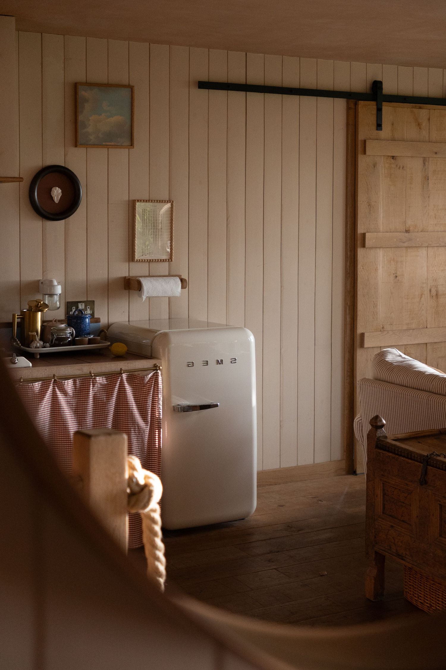 Cozy rustic cabin interior with a vintage SMEG refrigerator, wood-paneled walls, and a sliding barn door.