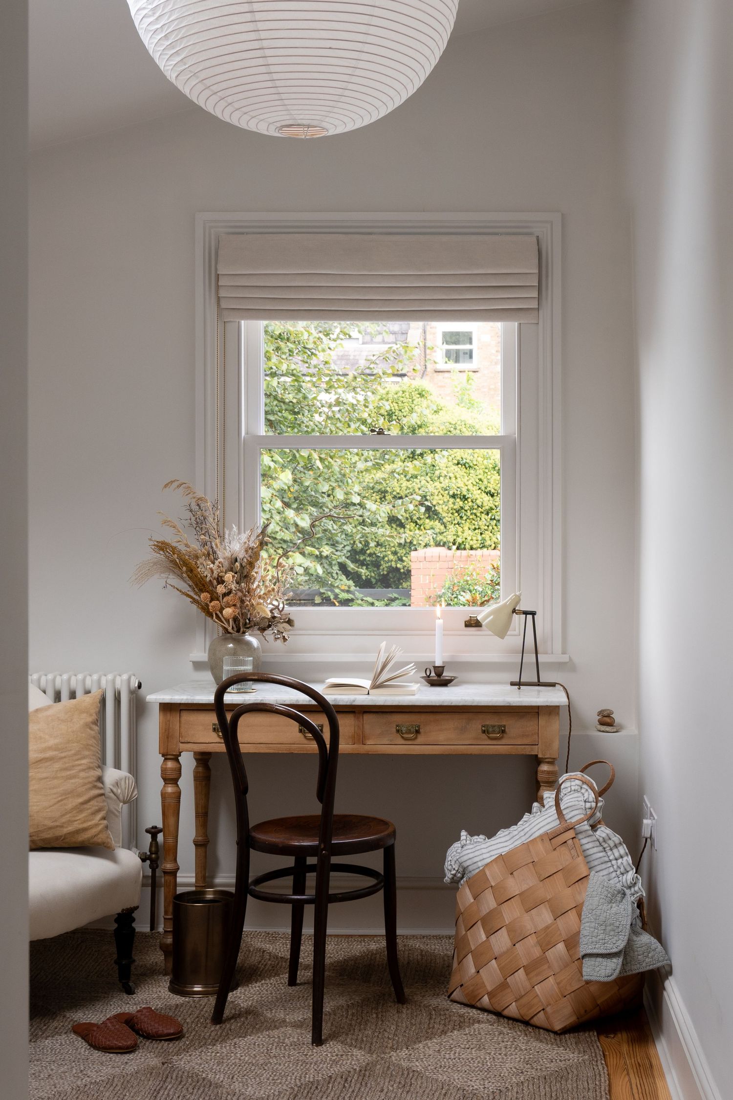 Cozy home office nook with vintage wooden desk, bentwood chair, dried flowers, and woven basket by window.