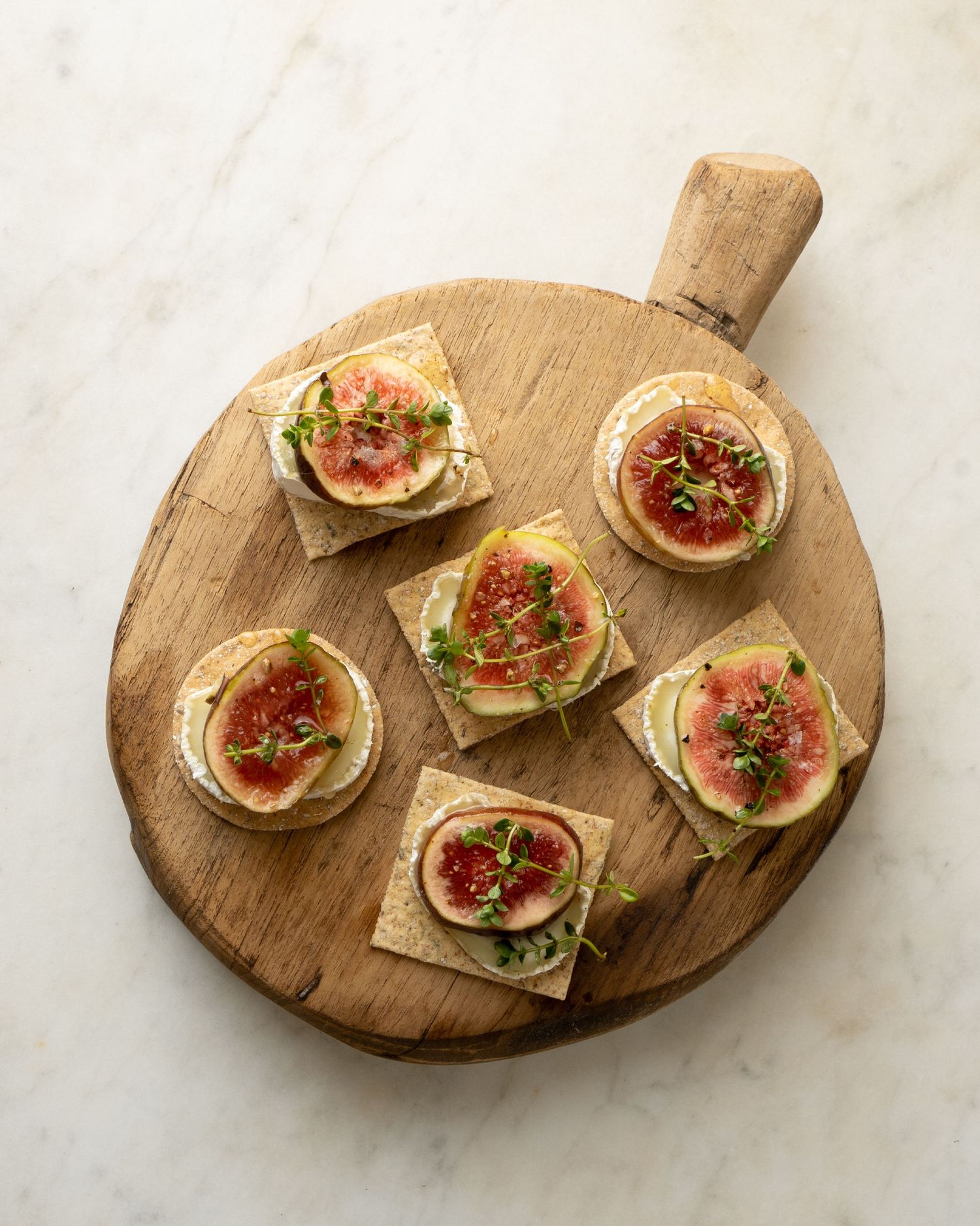 Crackers topped with brie, sliced fresh figs, and microgreens arranged on a round wooden board.