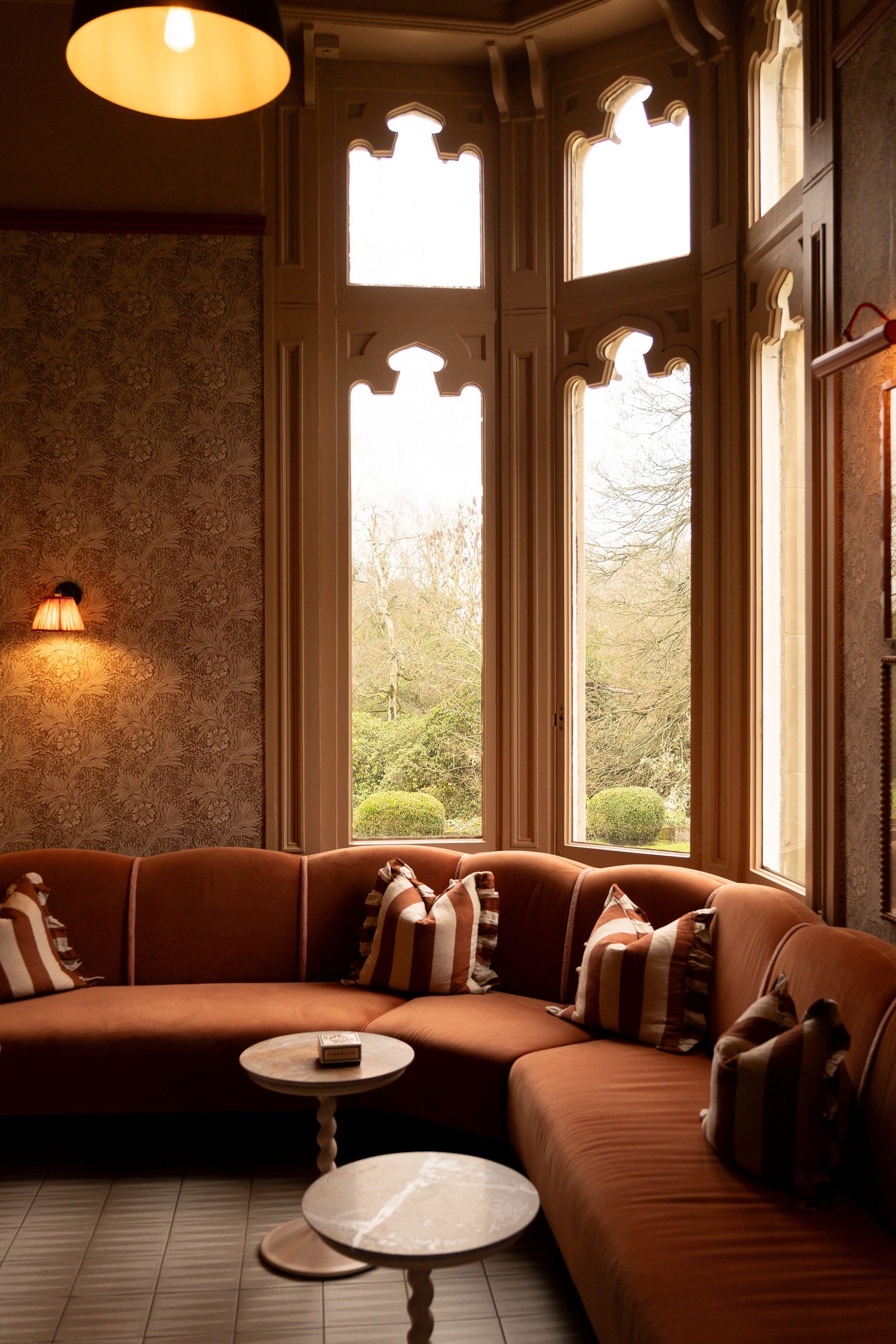 Luxurious rust velvet curved sectional sofa with striped pillows in a bay window alcove with Gothic arched windows.