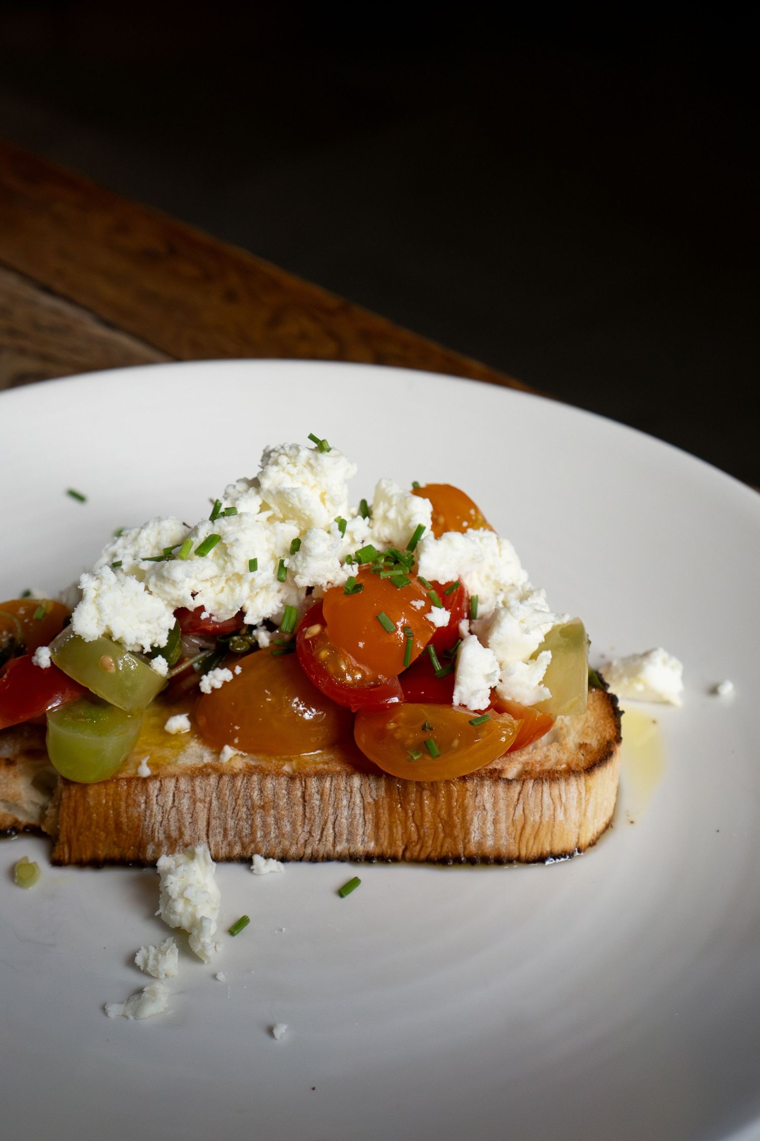 Rustic bruschetta topped with mixed cherry tomatoes, crumbled white cheese, and fresh herbs on toasted sourdough bread.