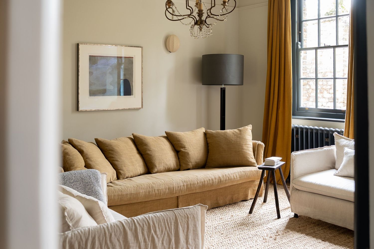 Cozy living room with tan linen sofa, mustard curtains, framed art, and a classic floor lamp.