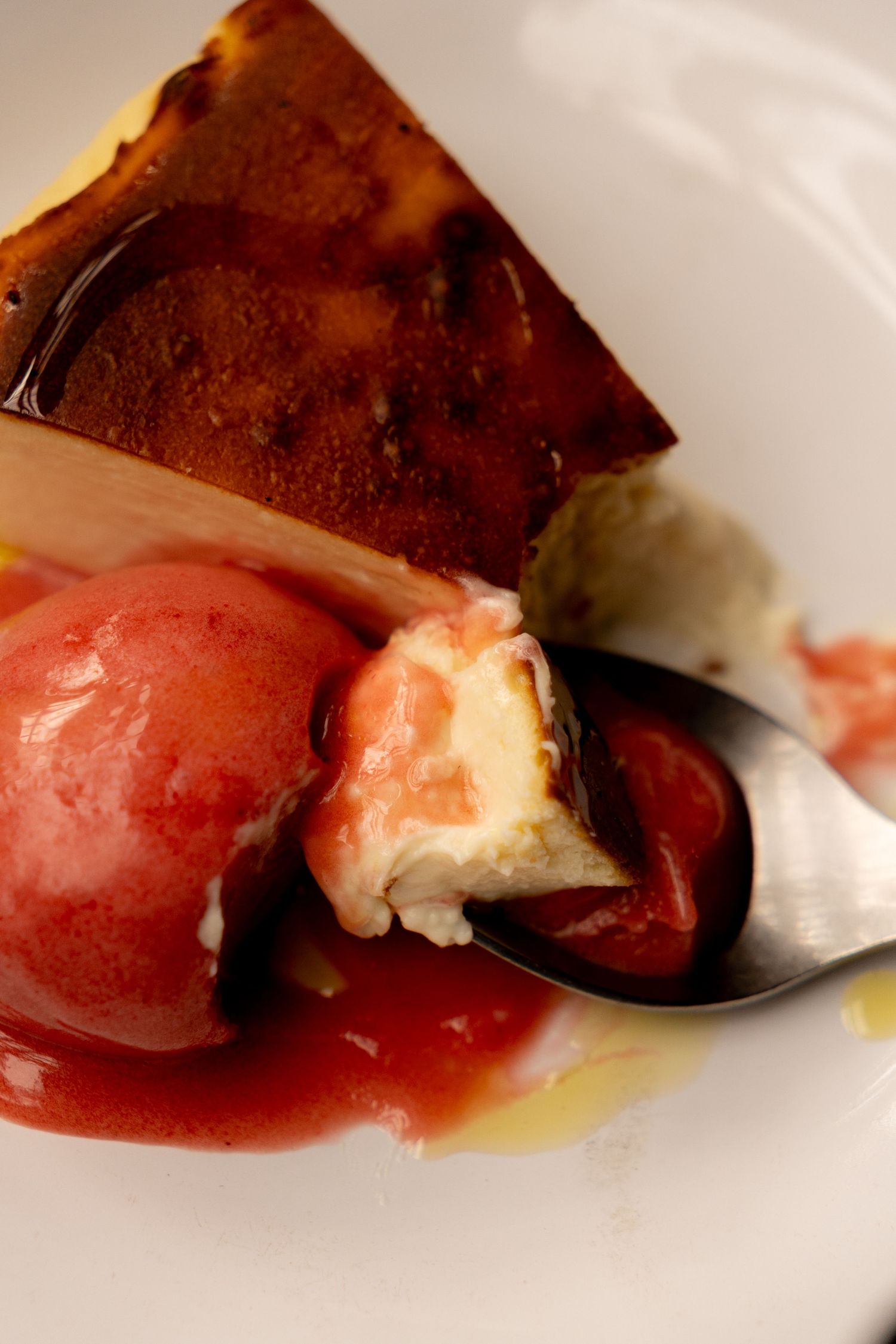 Close-up of a gourmet dessert with caramelized flan, pink sorbet, and cream on a white plate with a spoon.
