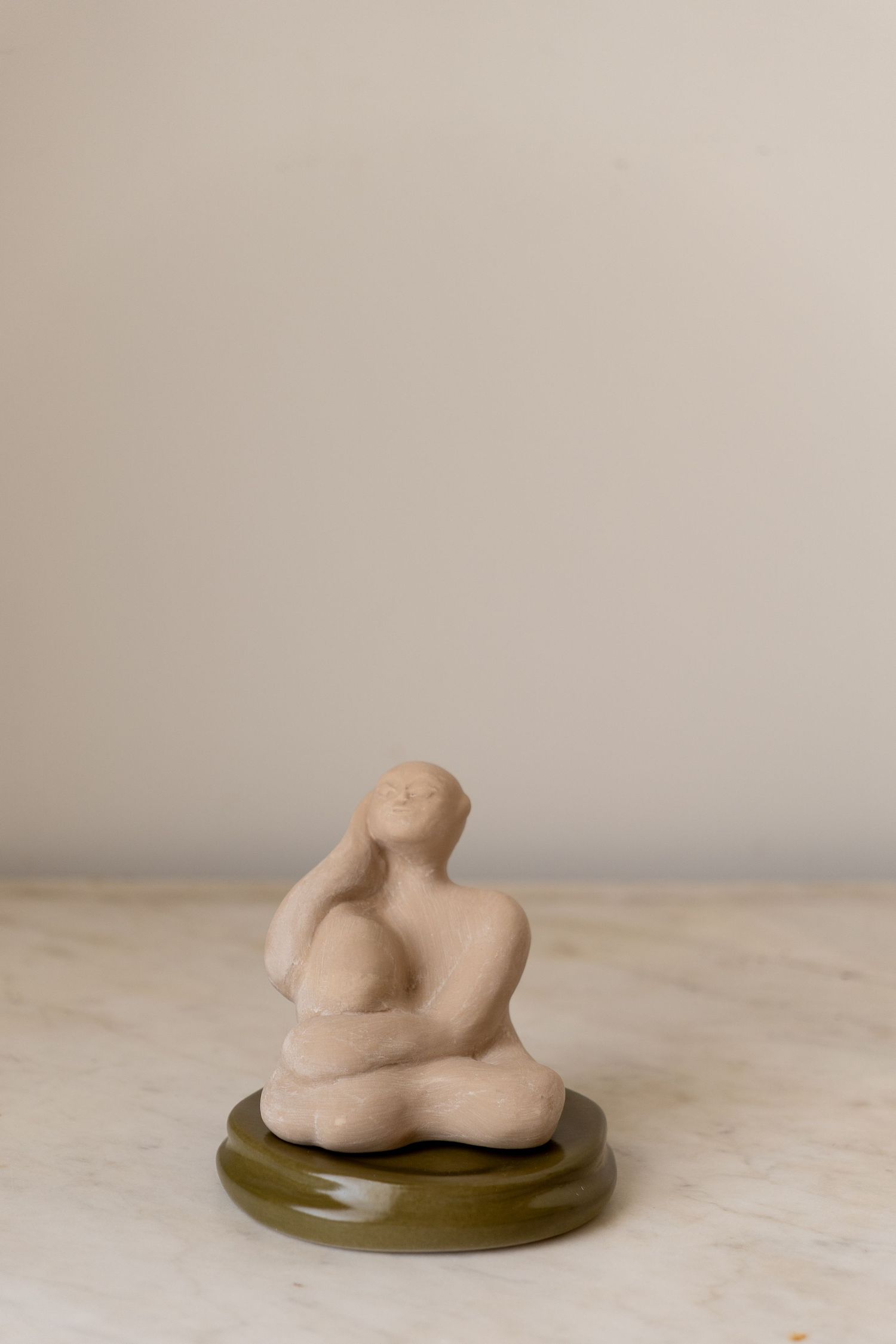 Small ceramic figurine of a seated person on a green glazed base on a marble surface.