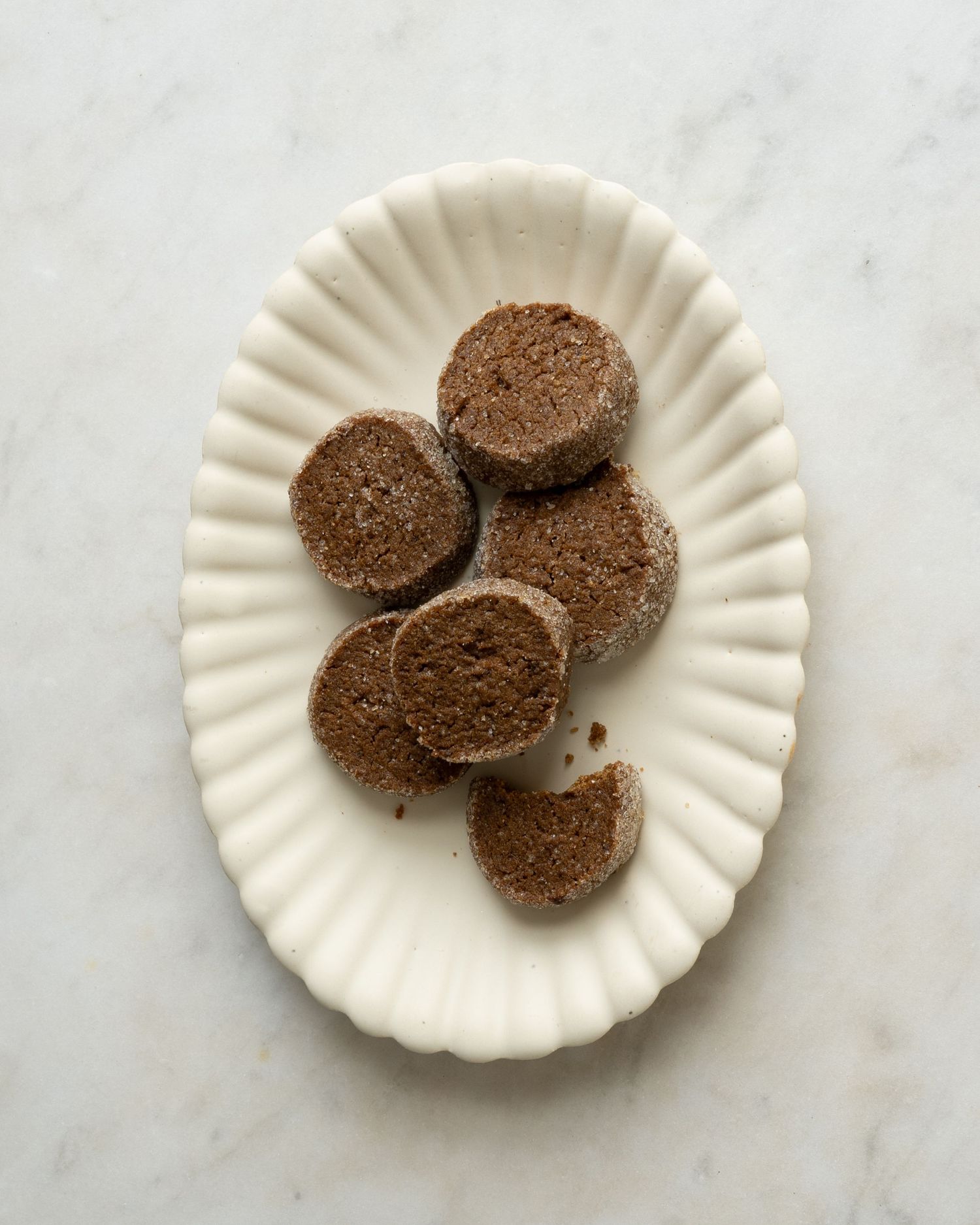 White oval dish with round chocolate shortbread cookies, one broken to reveal crumbly texture.