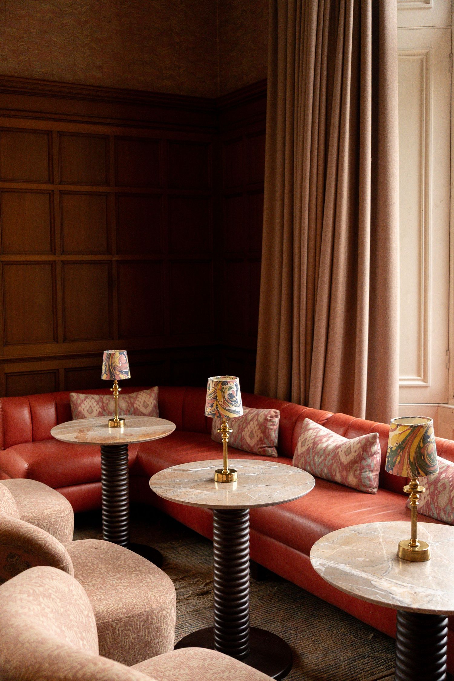 Sophisticated red leather curved banquette seating with marble pedestal tables and decorative brass lamps in a lounge.