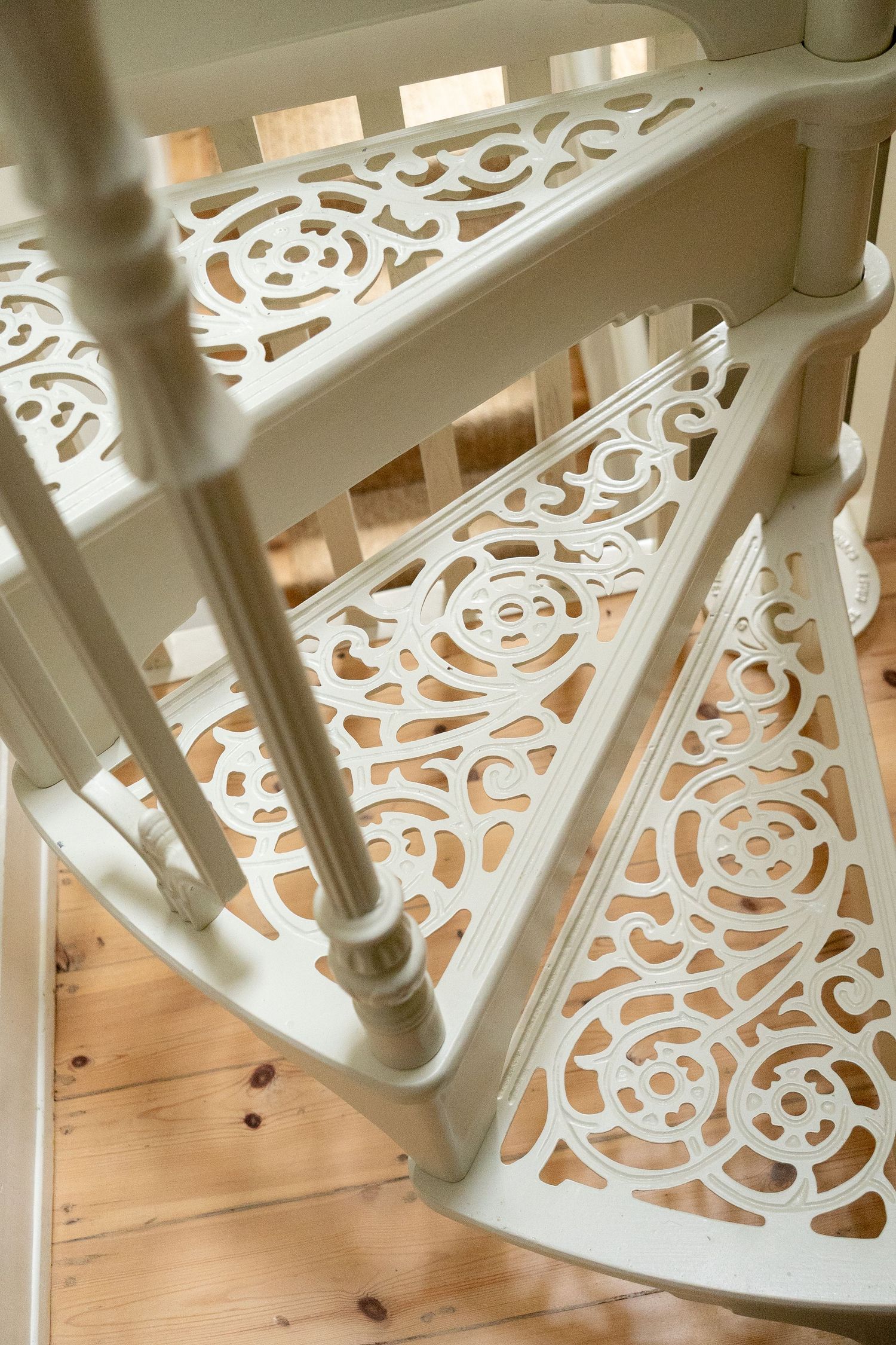 Close-up overhead view of ornate white cast iron spiral staircase with floral pattern treads.