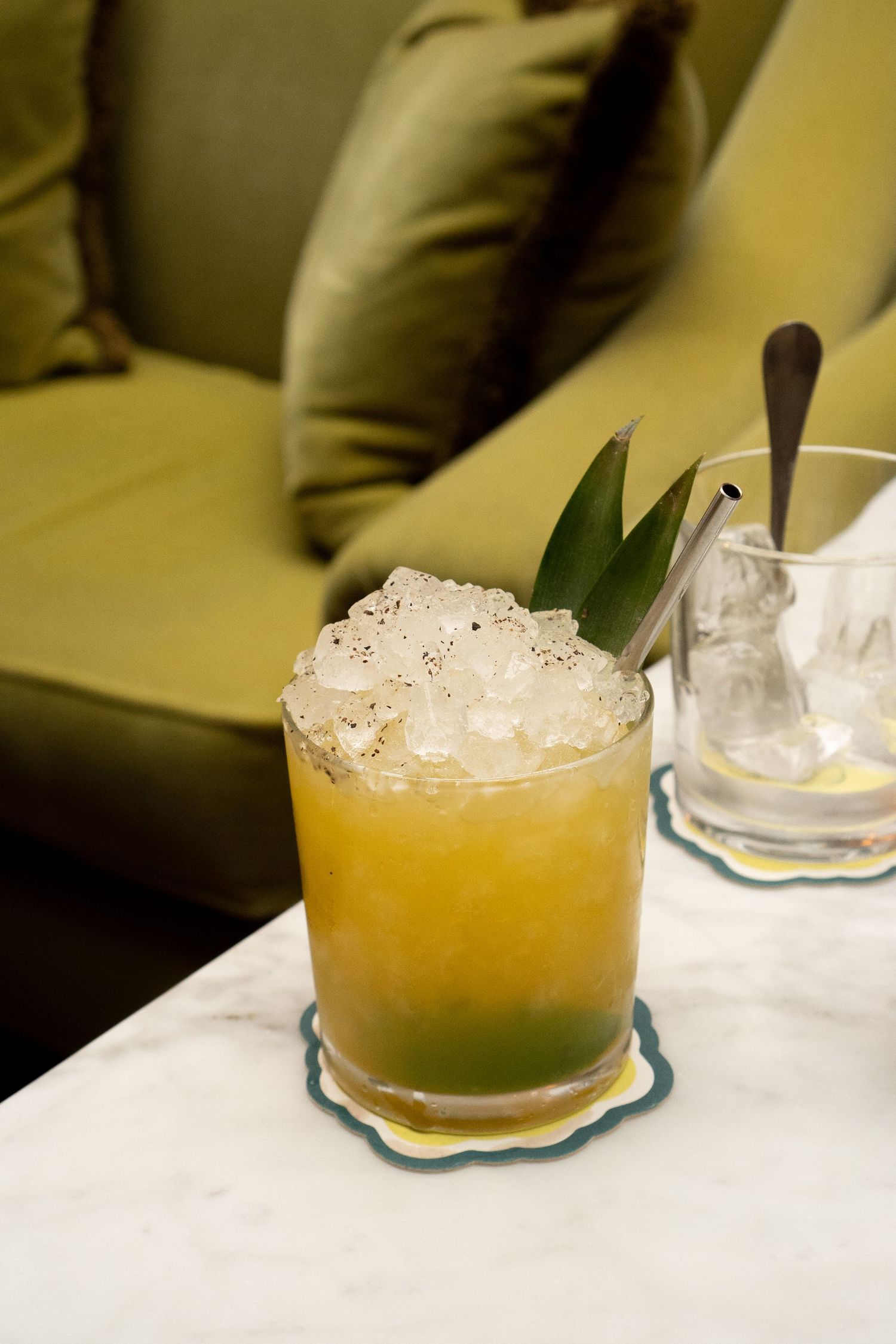 Tropical cocktail with crushed ice, pineapple leaf garnish, and golden hue served on a marble surface.