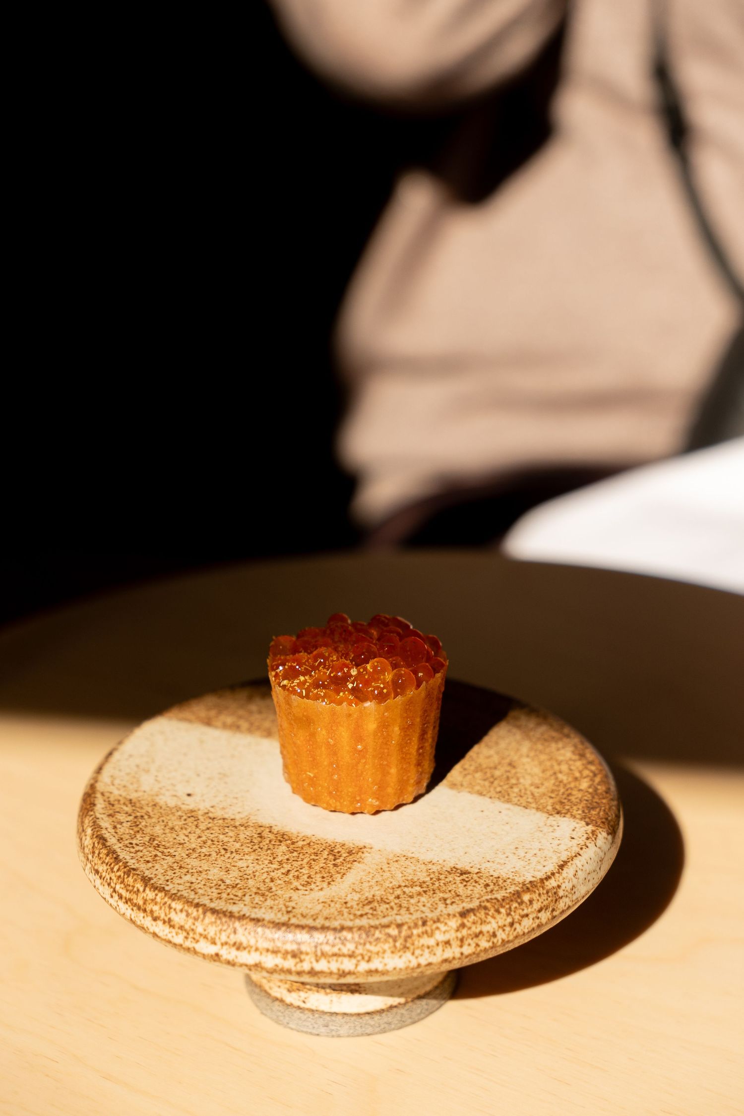 Elegant canele pastry topped with salmon roe caviar presented on ceramic pedestal in restaurant.