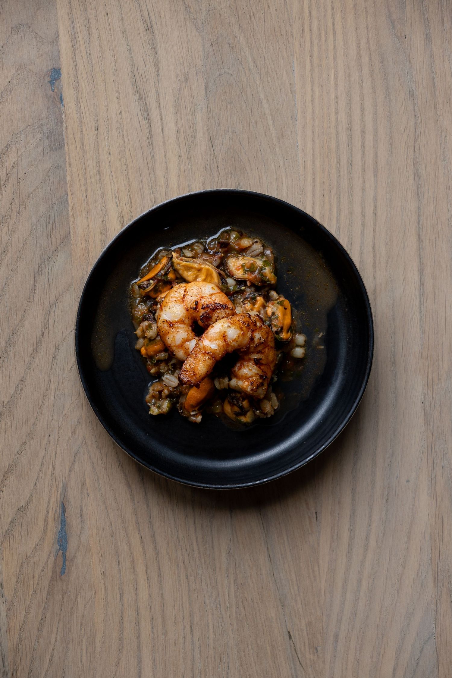 Gourmet sautéed shrimp with herbs and sauce served on a black plate on a wooden surface.