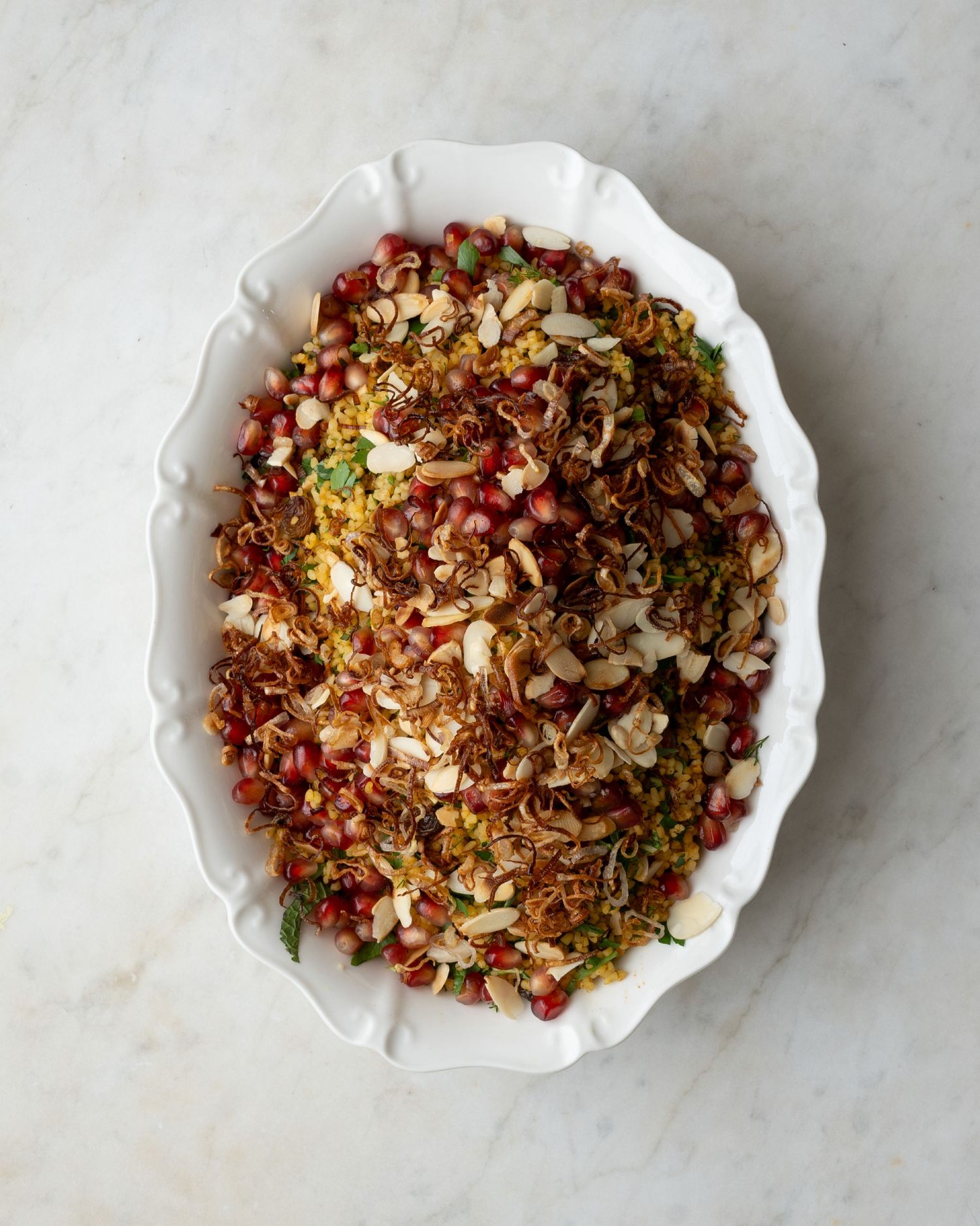 White oval dish filled with saffron rice topped with toasted almonds, pomegranate seeds, and herbs.