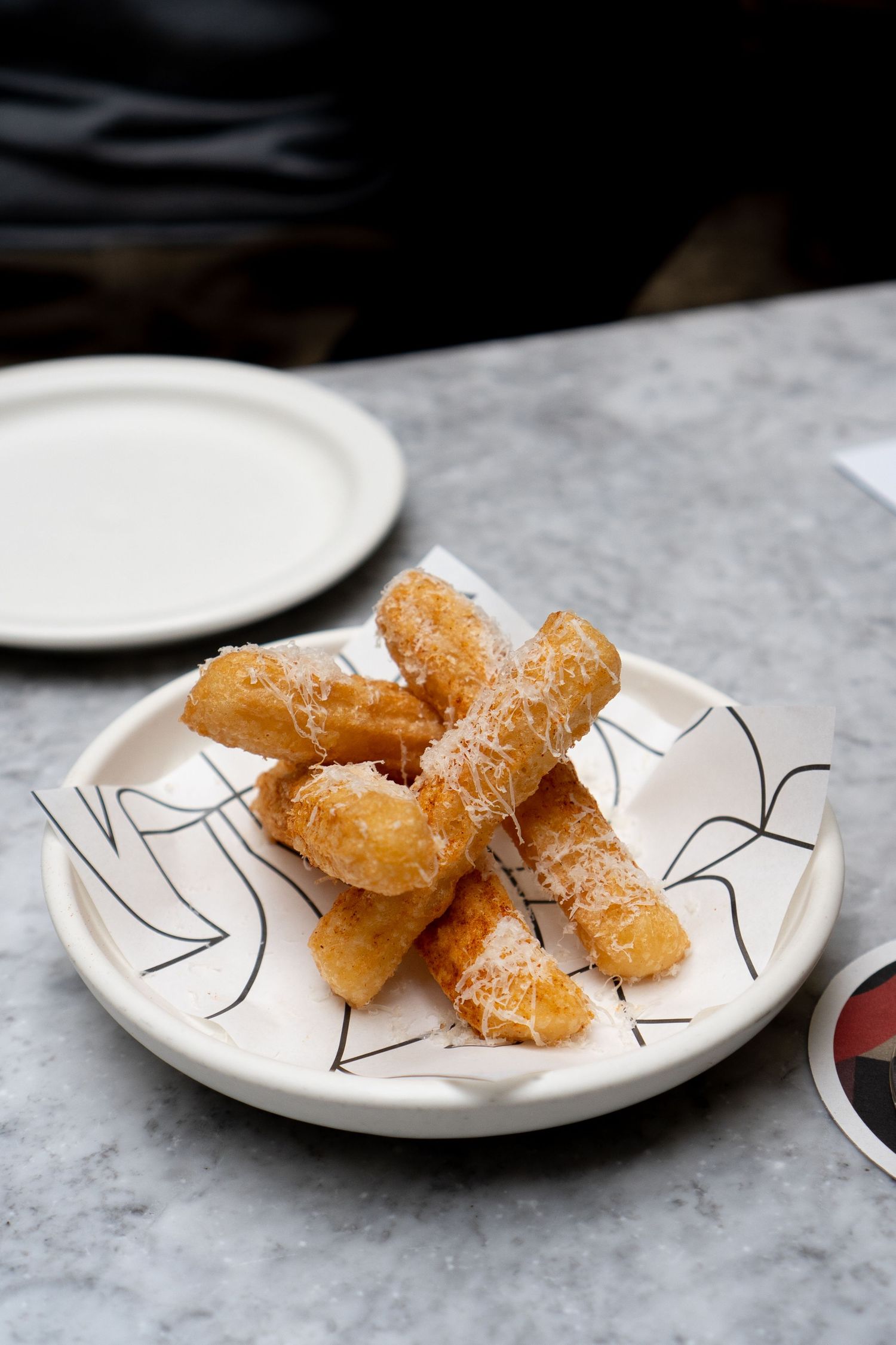 Golden fried breadsticks dusted with parmesan cheese served on decorative plate on marble table.
