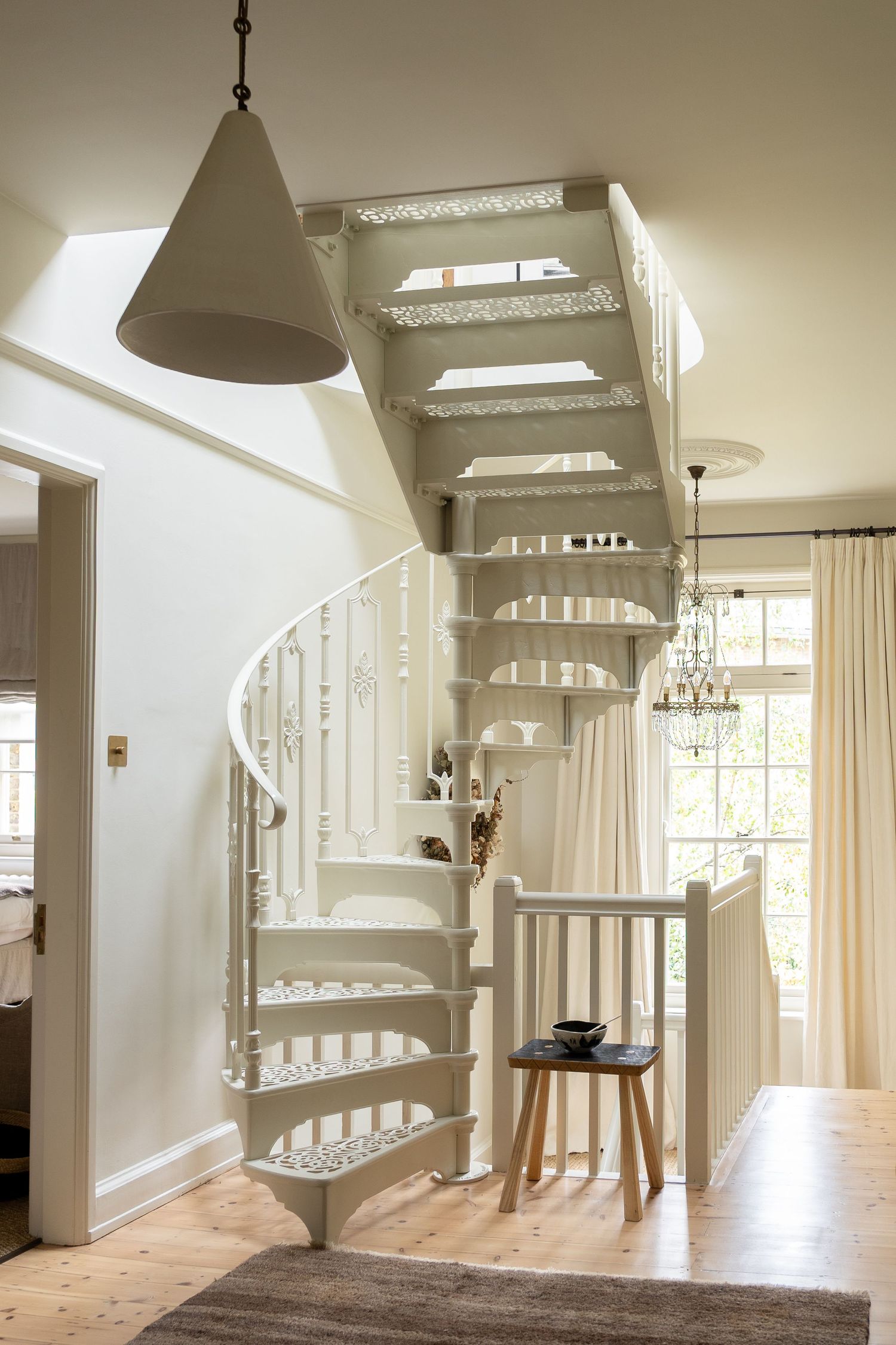 White spiral staircase with ornate cast iron details in a bright Scandinavian-style living room with wood floors.