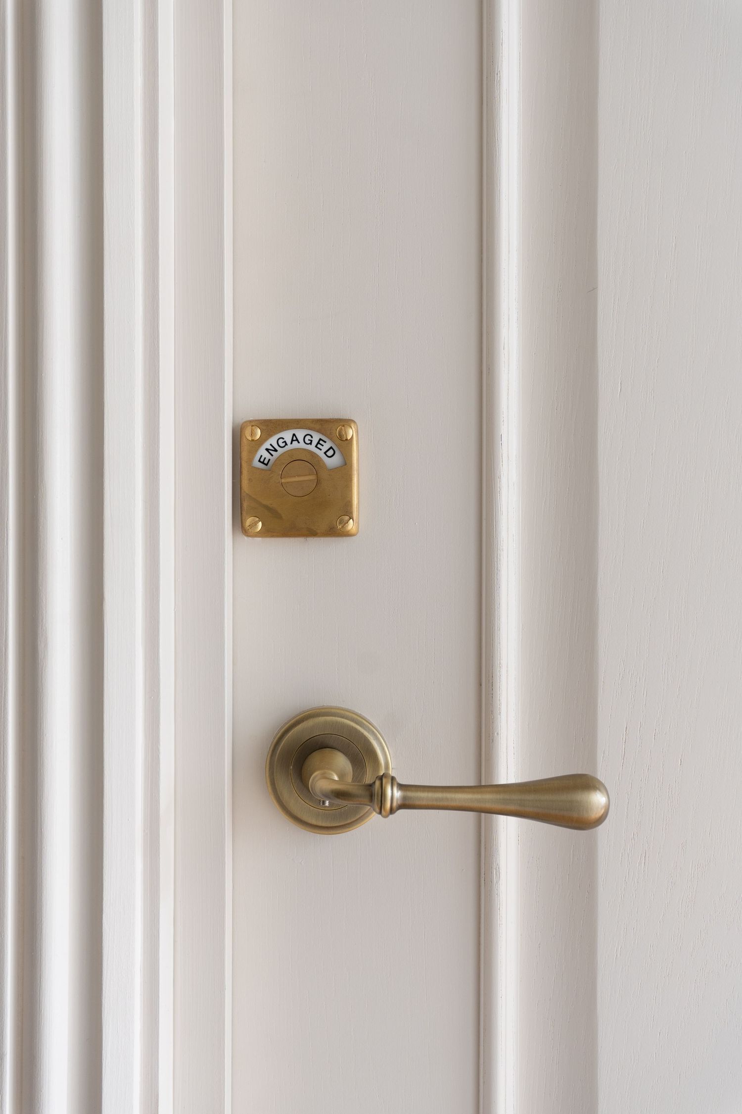 White paneled door with antique brass lever handle and engaged lock indicator plate.