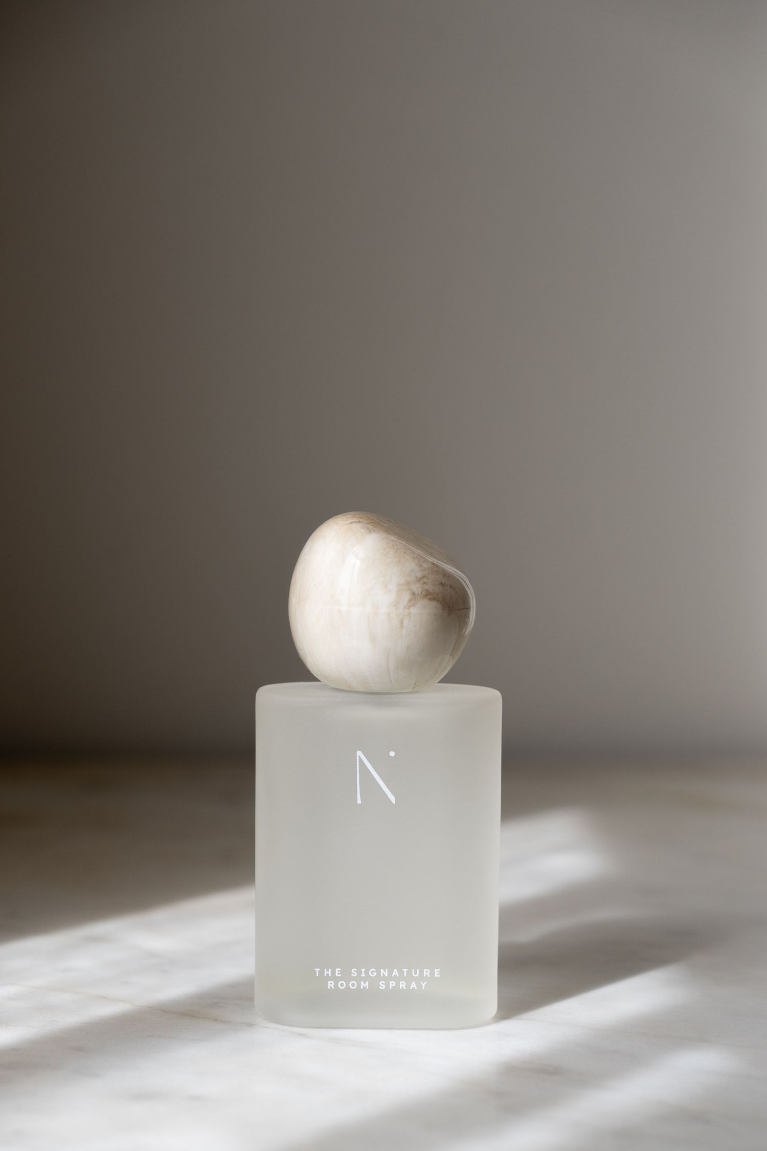 N. Signature Room Spray in frosted square glass bottle with round marble stone cap on white marble surface.