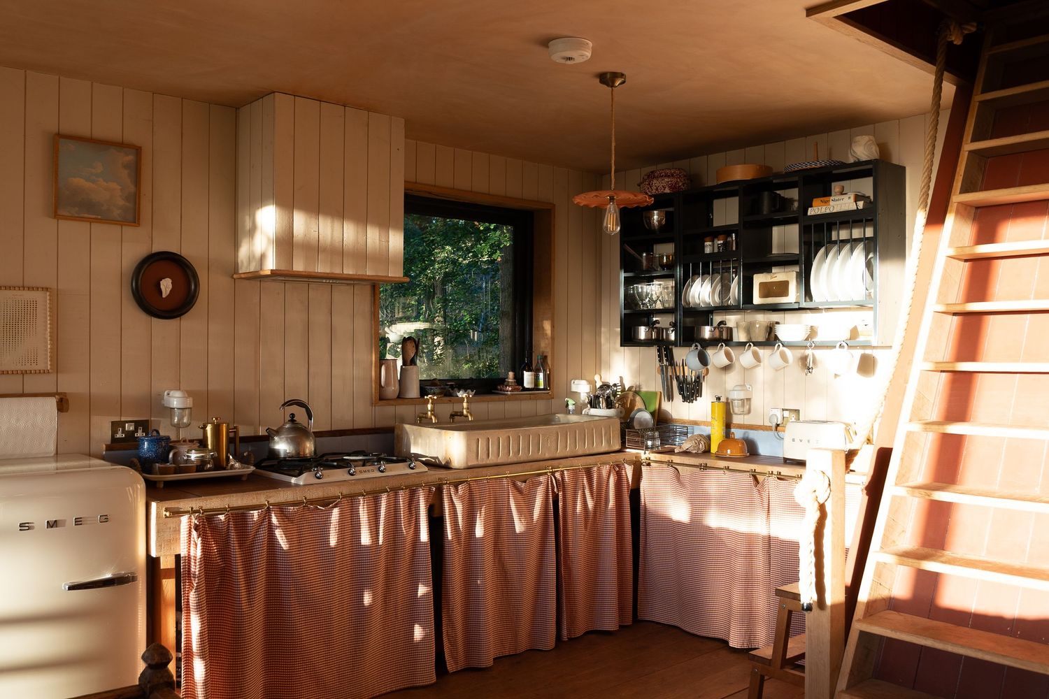 Charming small kitchen with pink curtained cabinets, open shelving, and a vintage white stove in a wooden cabin.
