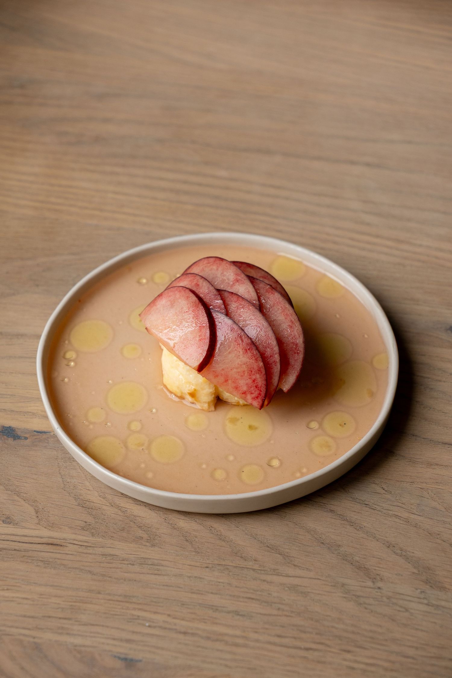 Elegant plated dessert with thinly sliced peaches on a cream ceramic plate, drizzled with golden syrup on a wooden table.