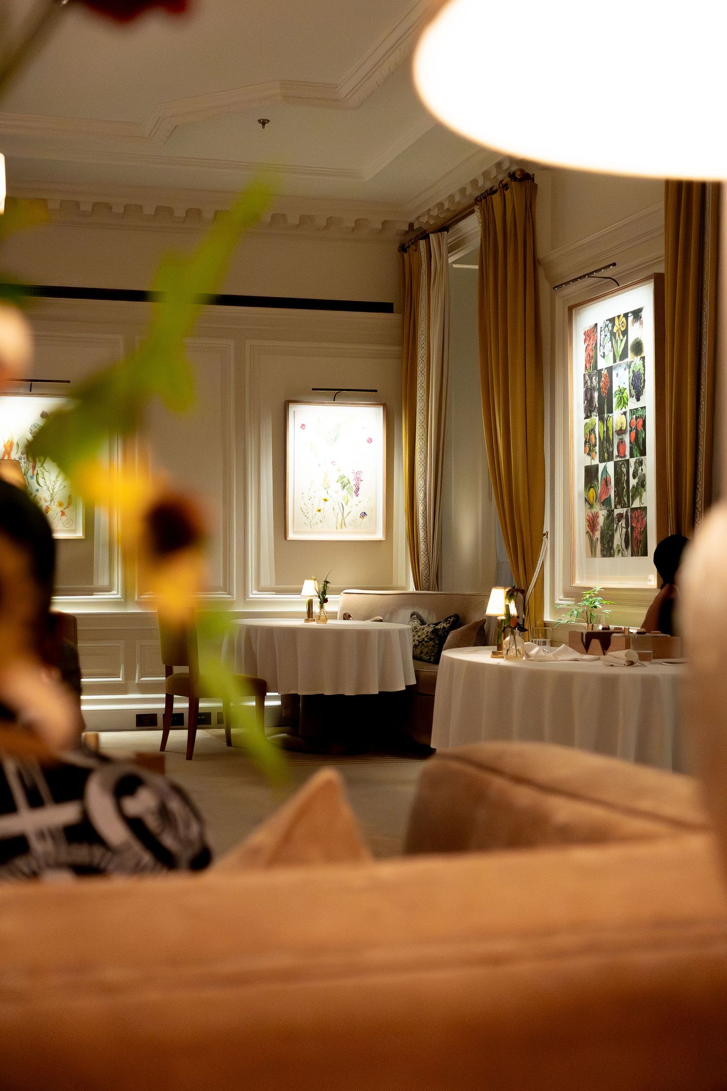 Elegant fine dining restaurant interior with white tablecloths, gold drapes, and artwork on paneled walls.