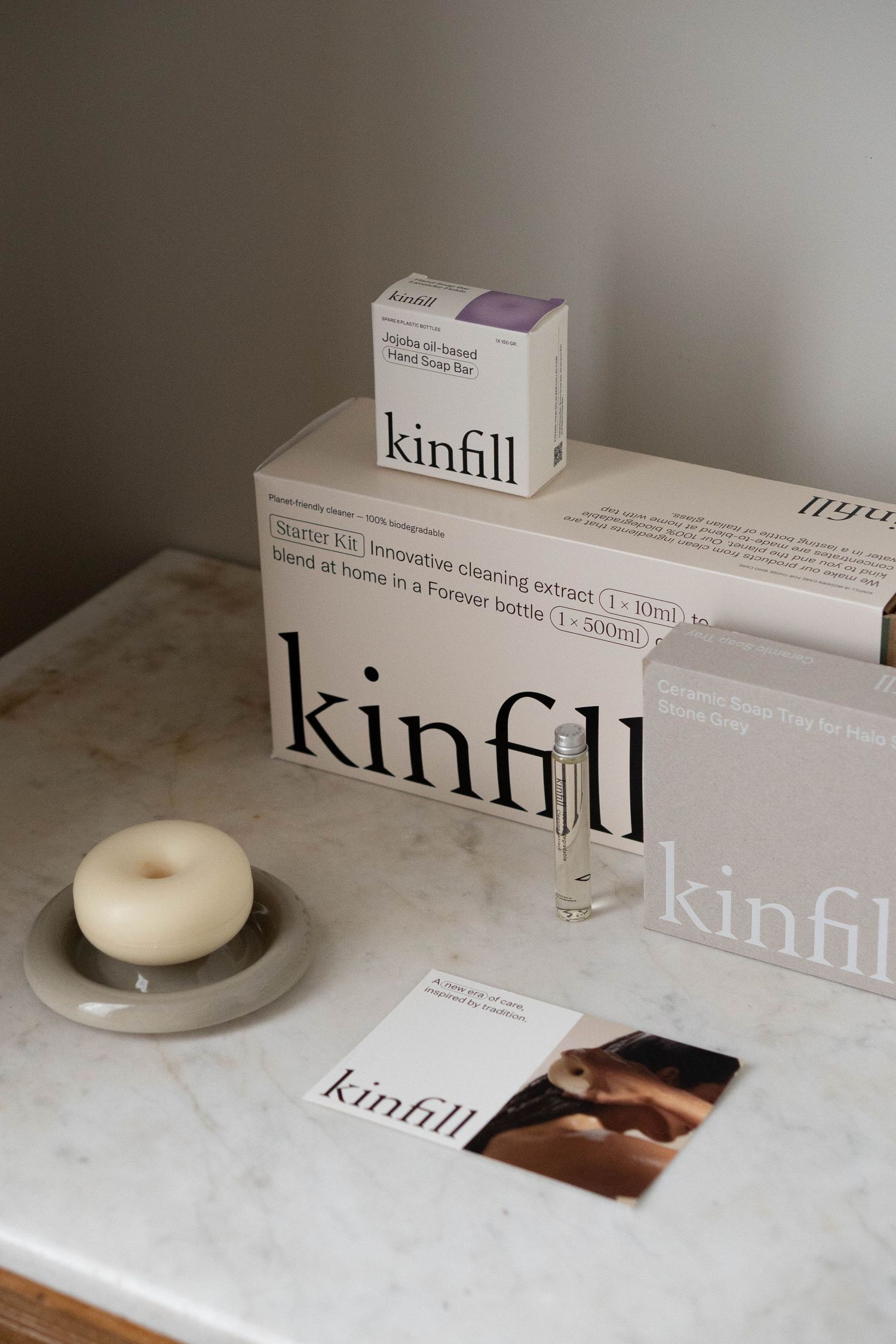 Kinfill cleaning products displayed on marble surface with candle, featuring refillable bottles and eco-friendly packaging.