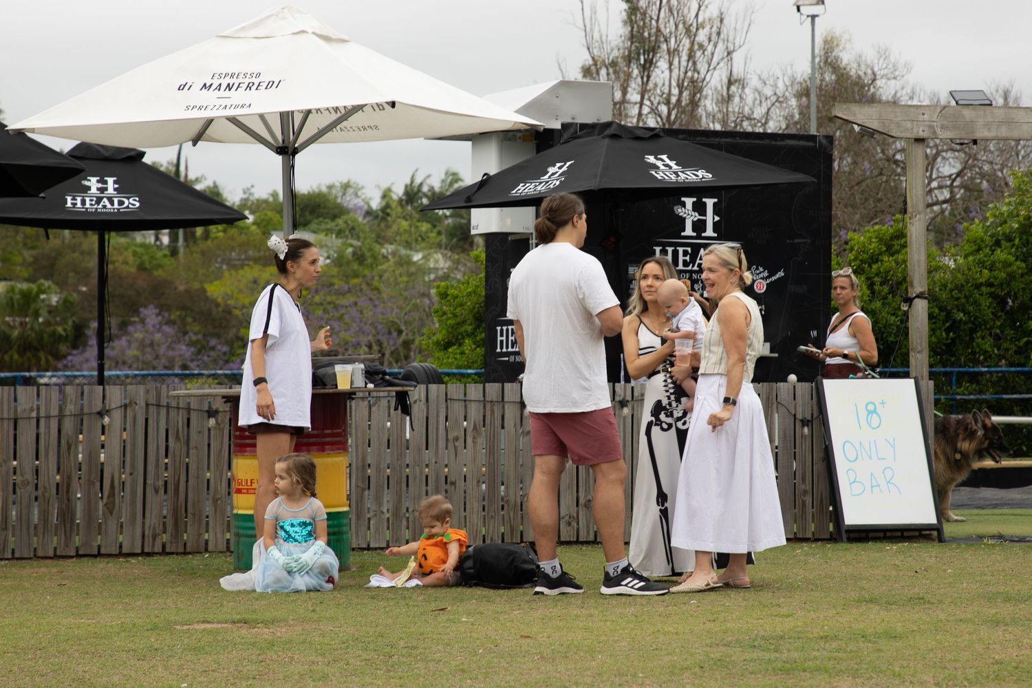 Families with young children relax on grass at an outdoor Halloween community festival event.
