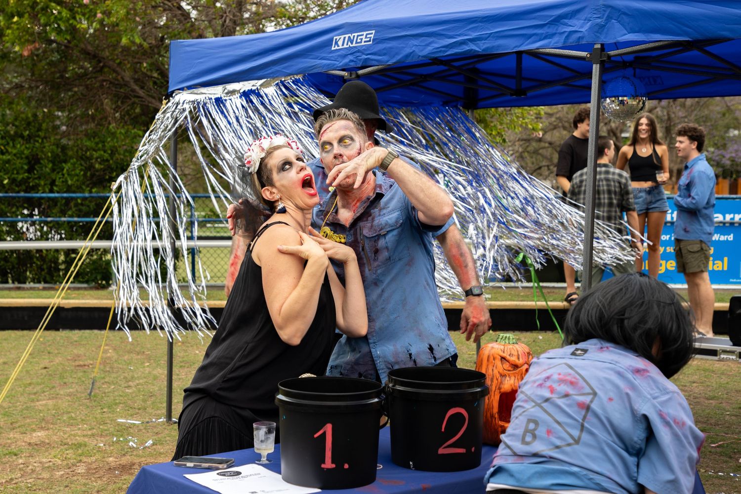 Couple in zombie Halloween costumes posing at a festival booth.