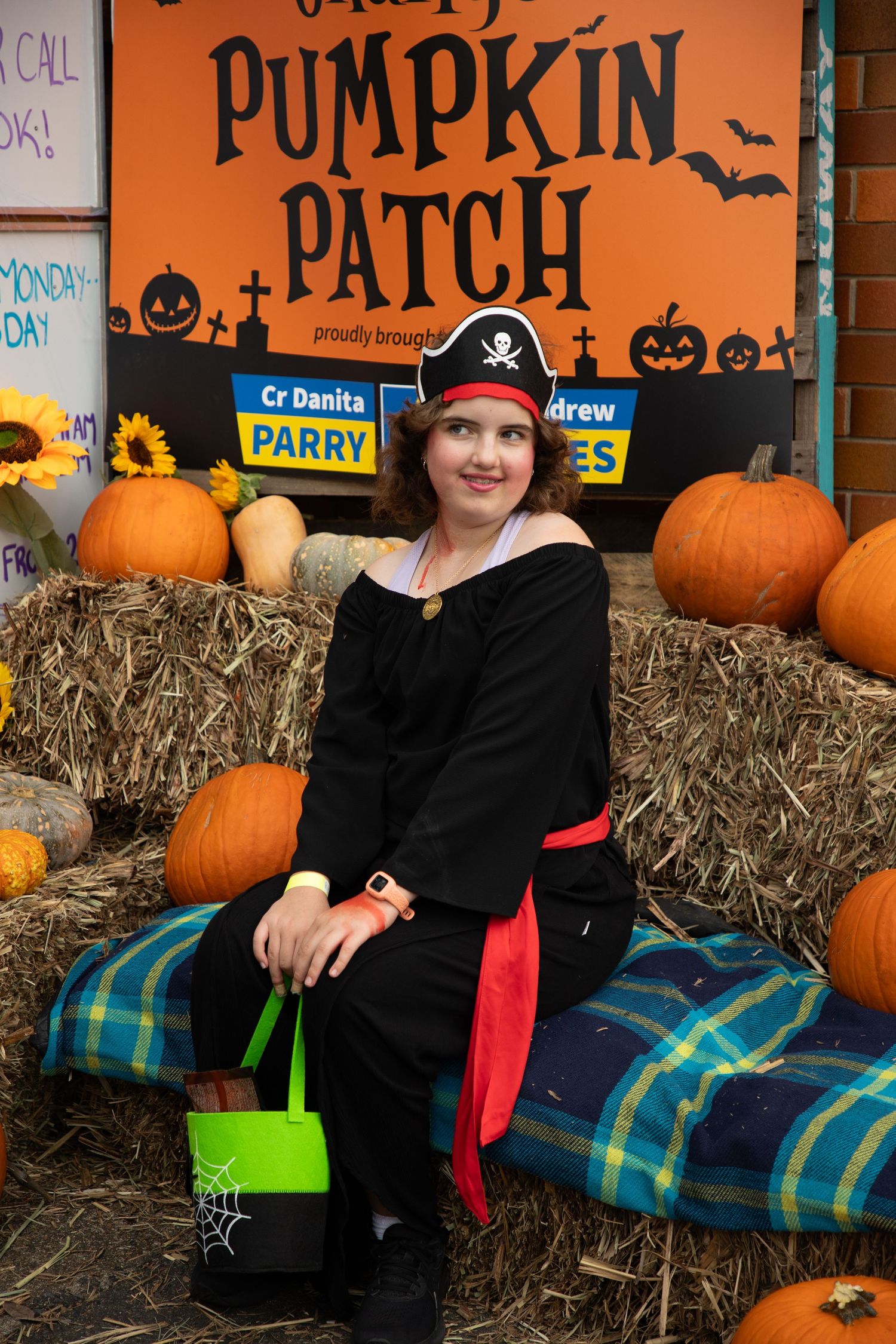 Woman dressed as a pirate sits on hay bales at a Halloween pumpkin patch display with orange pumpkins.