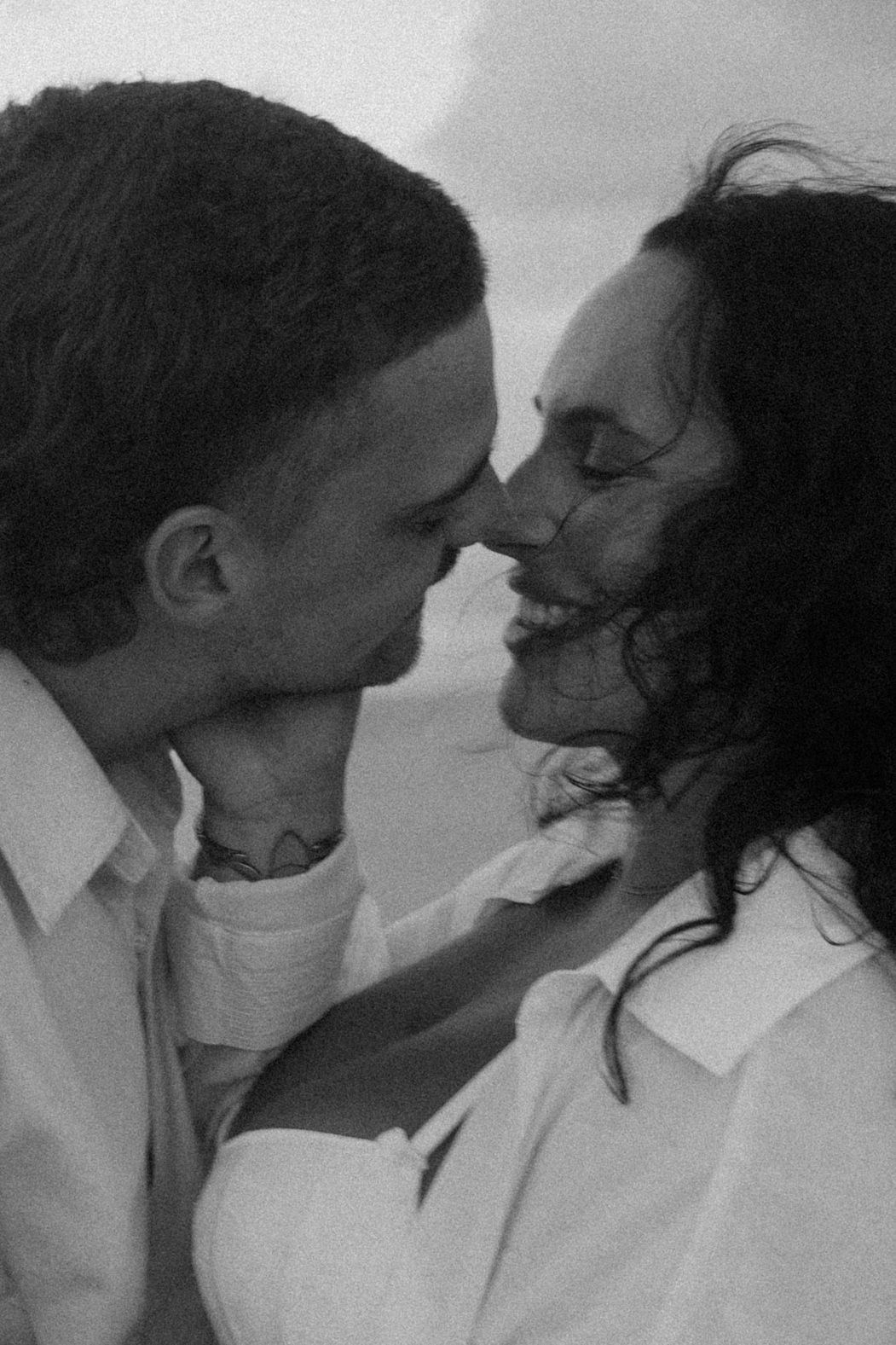 Black and white photo of a romantic couple sharing an intimate moment, nearly kissing outdoors.