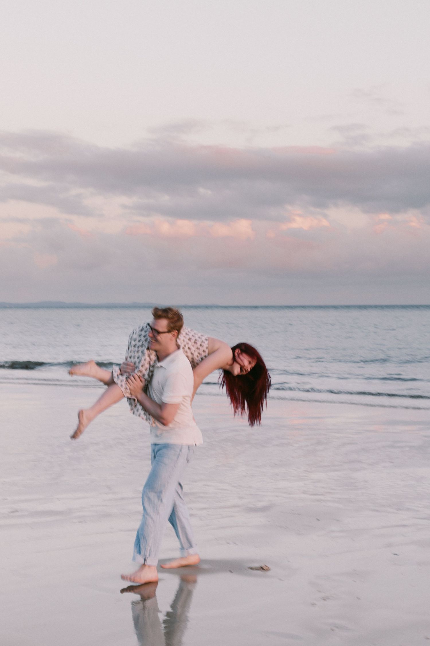 Joyful couple playing on a sandy beach at sunset, man spinning woman in his arms.