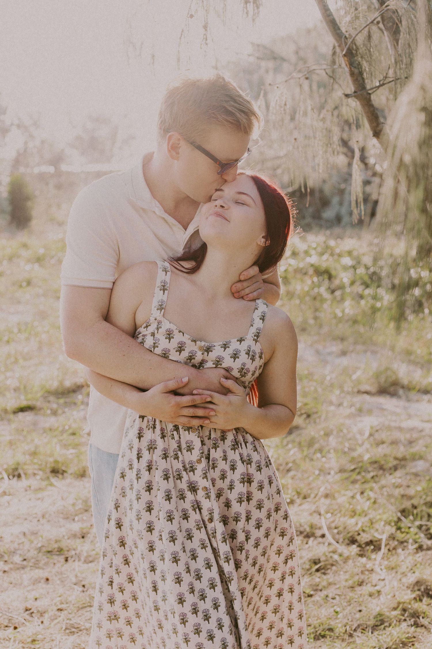 Man tenderly kissing woman on the cheek while embracing her in a sunny outdoor setting.