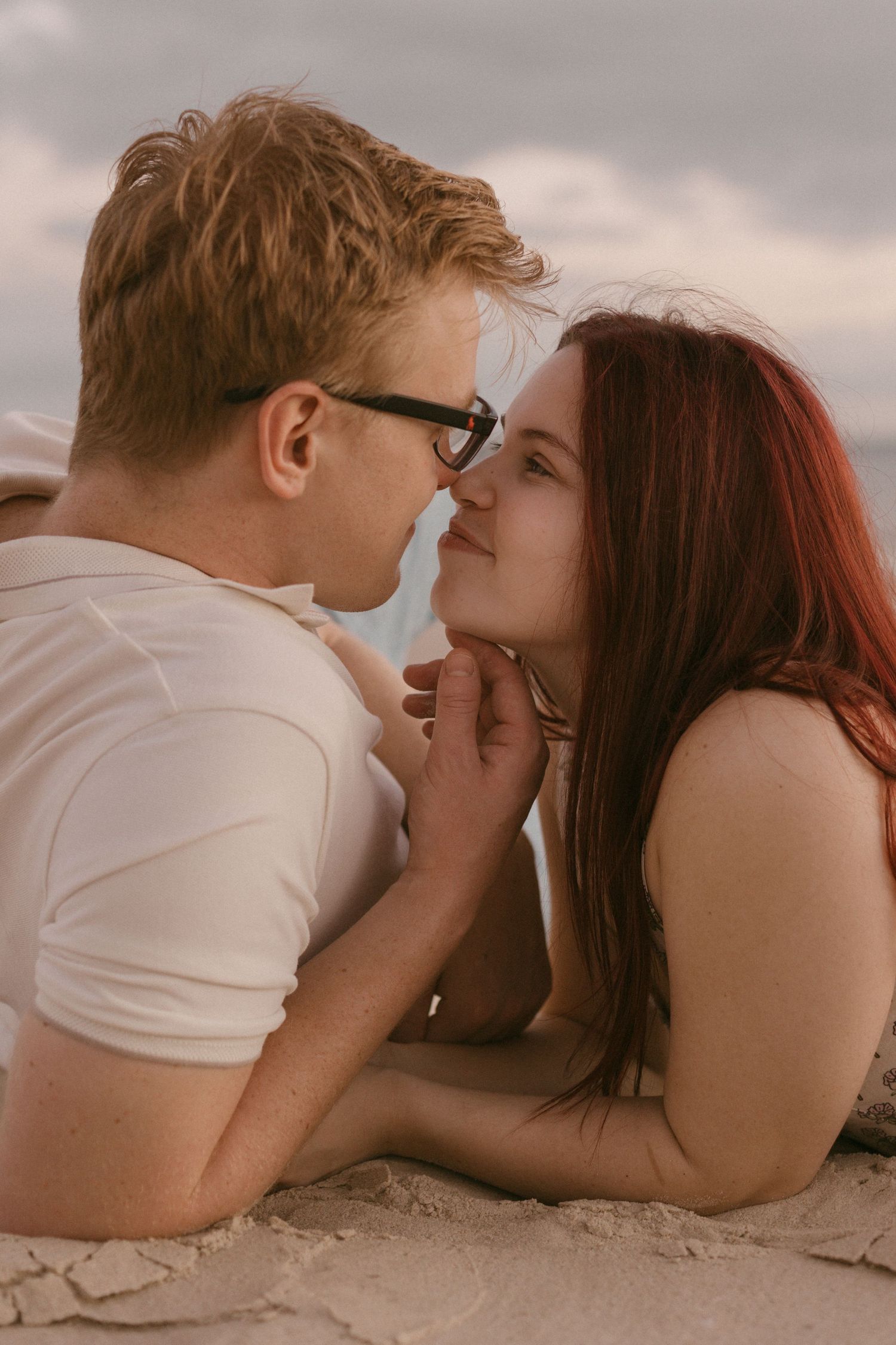 Couple lying on beach sand gazing into each others eyes romantically at sunset.