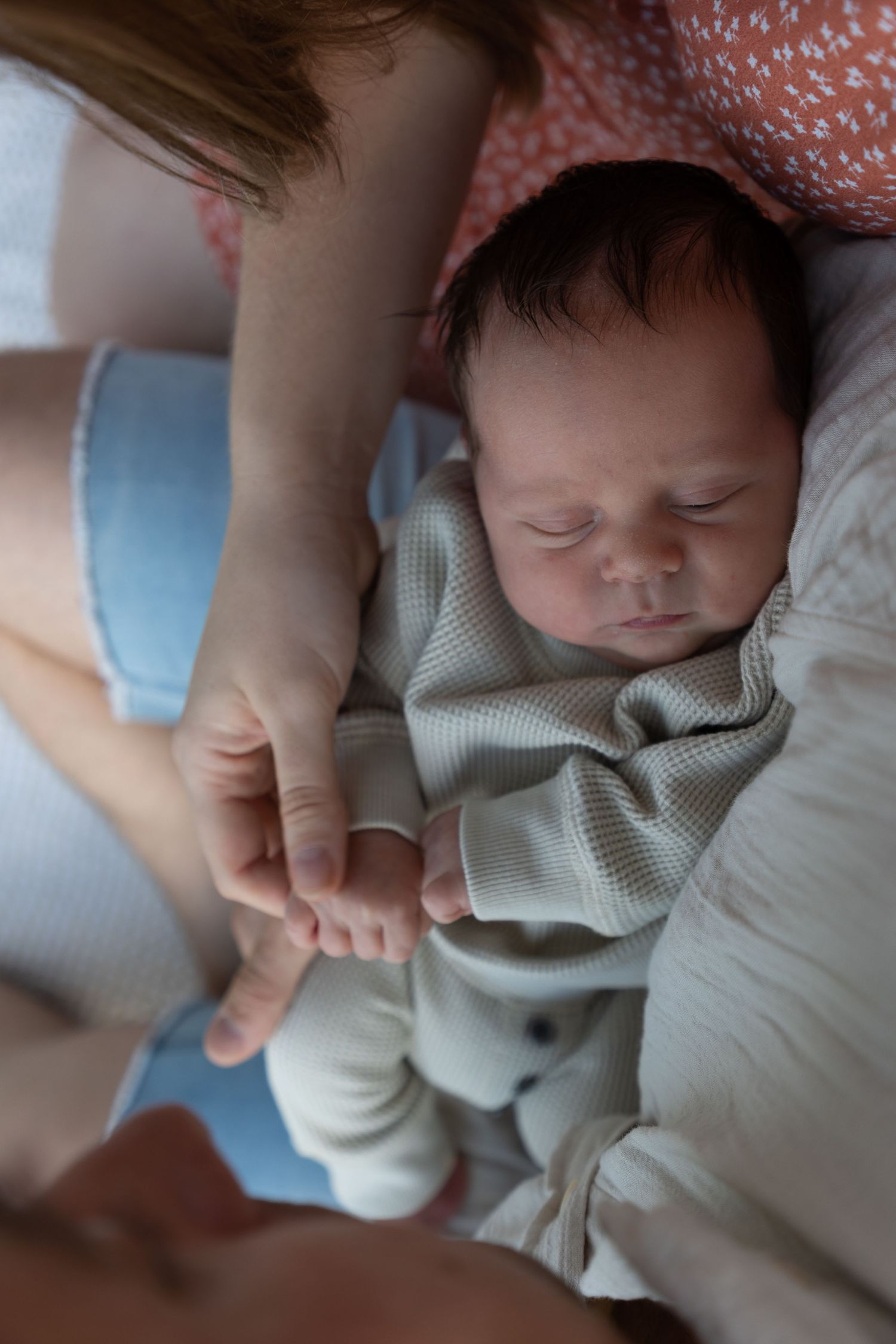 Newborn baby sleeping peacefully while mother gently holds tiny hand in soft natural light.