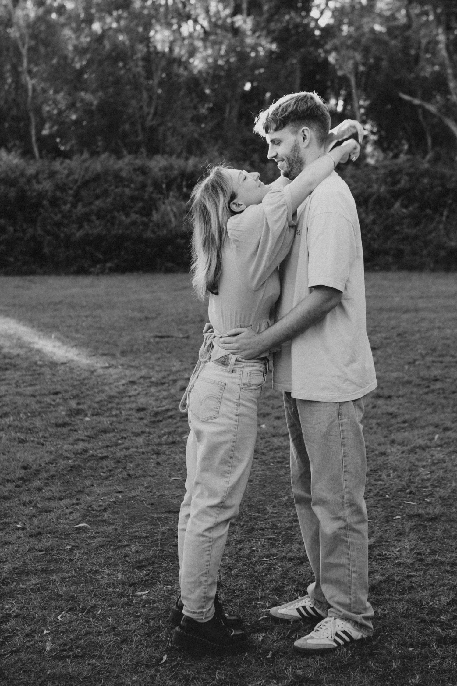 Black and white photo of a romantic couple embracing and gazing at each other in a grassy outdoor setting.