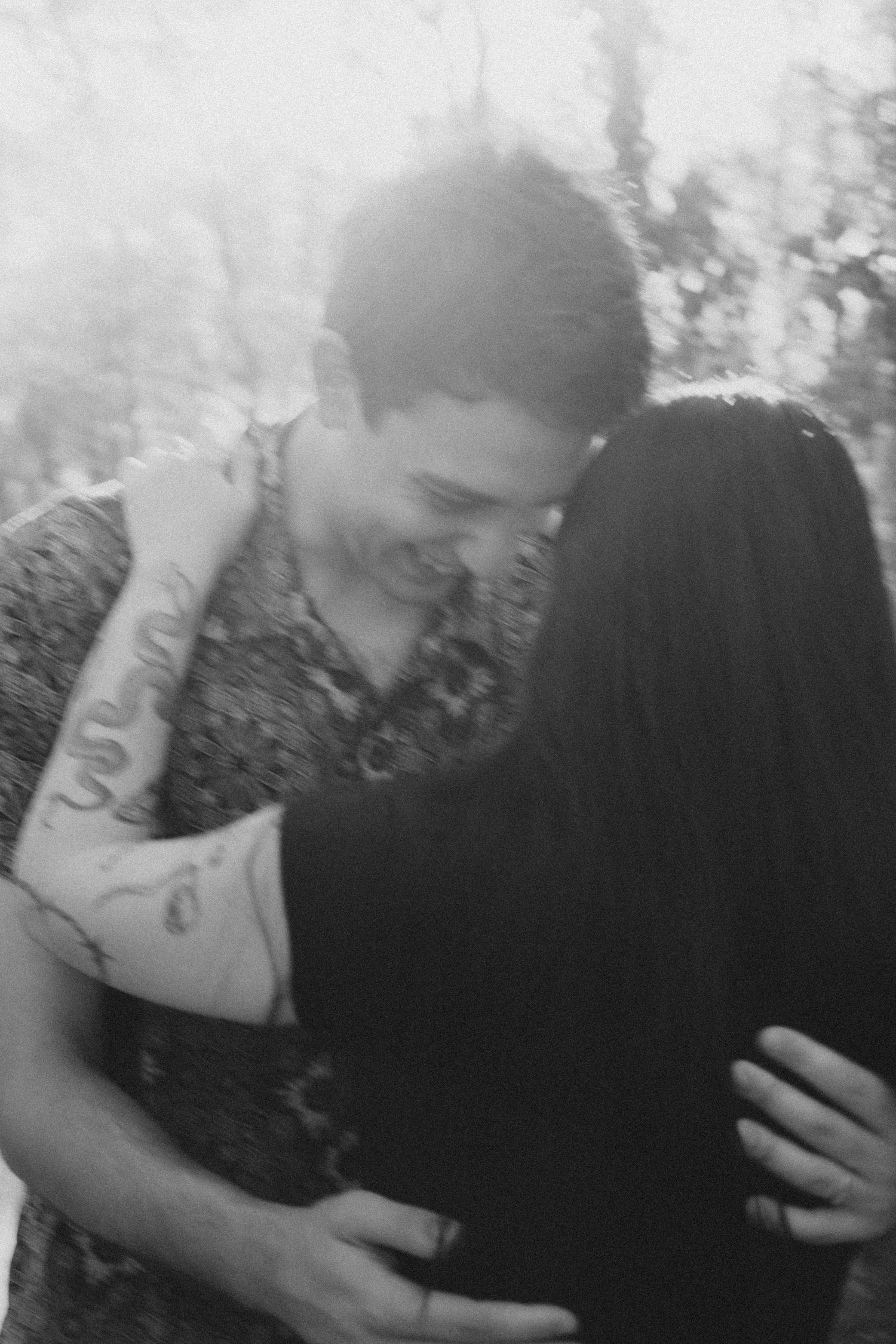 Black and white close-up of a couple sharing a tender embrace among trees in a forest.