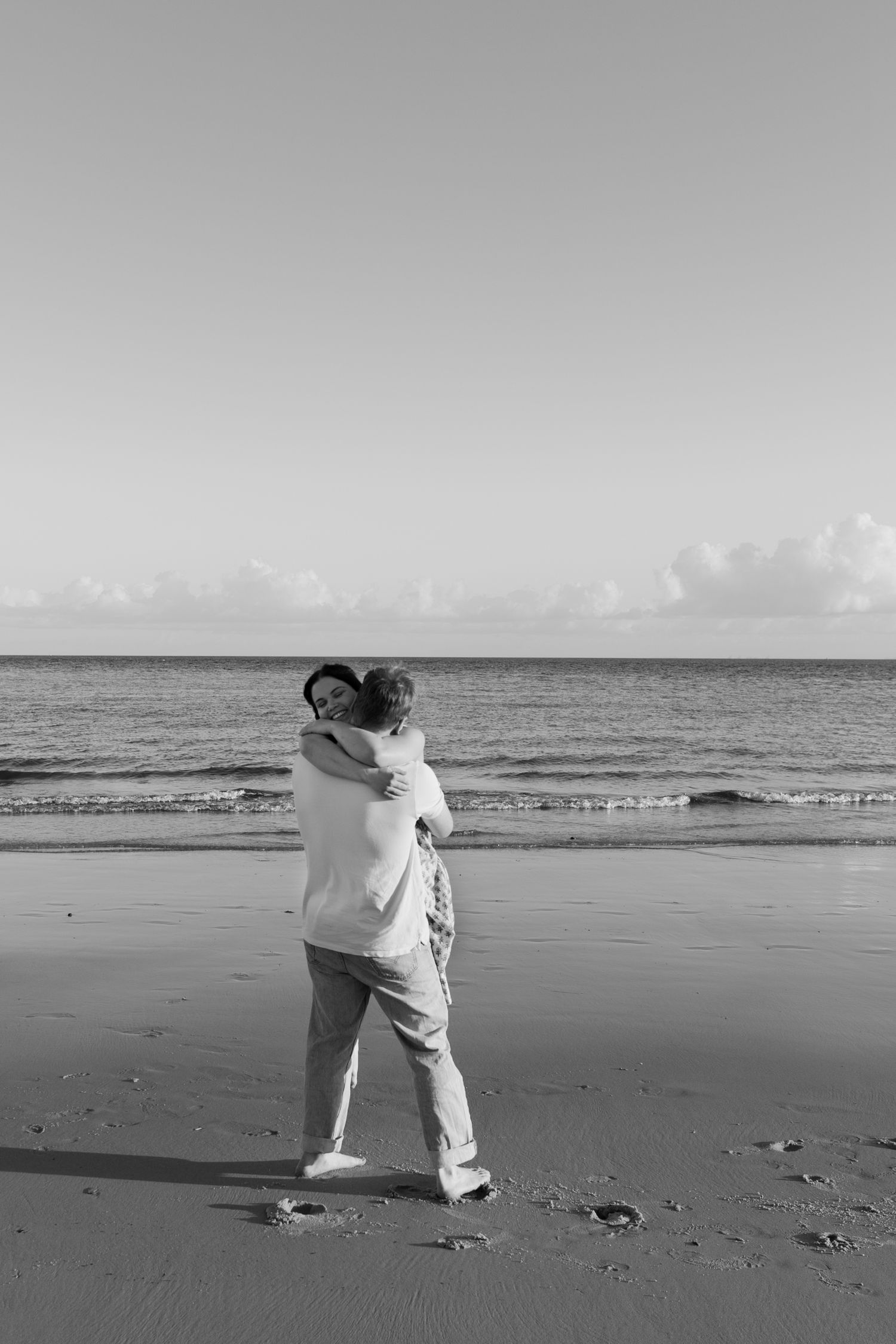 A couple embraces romantically on a serene beach in this black and white photo.