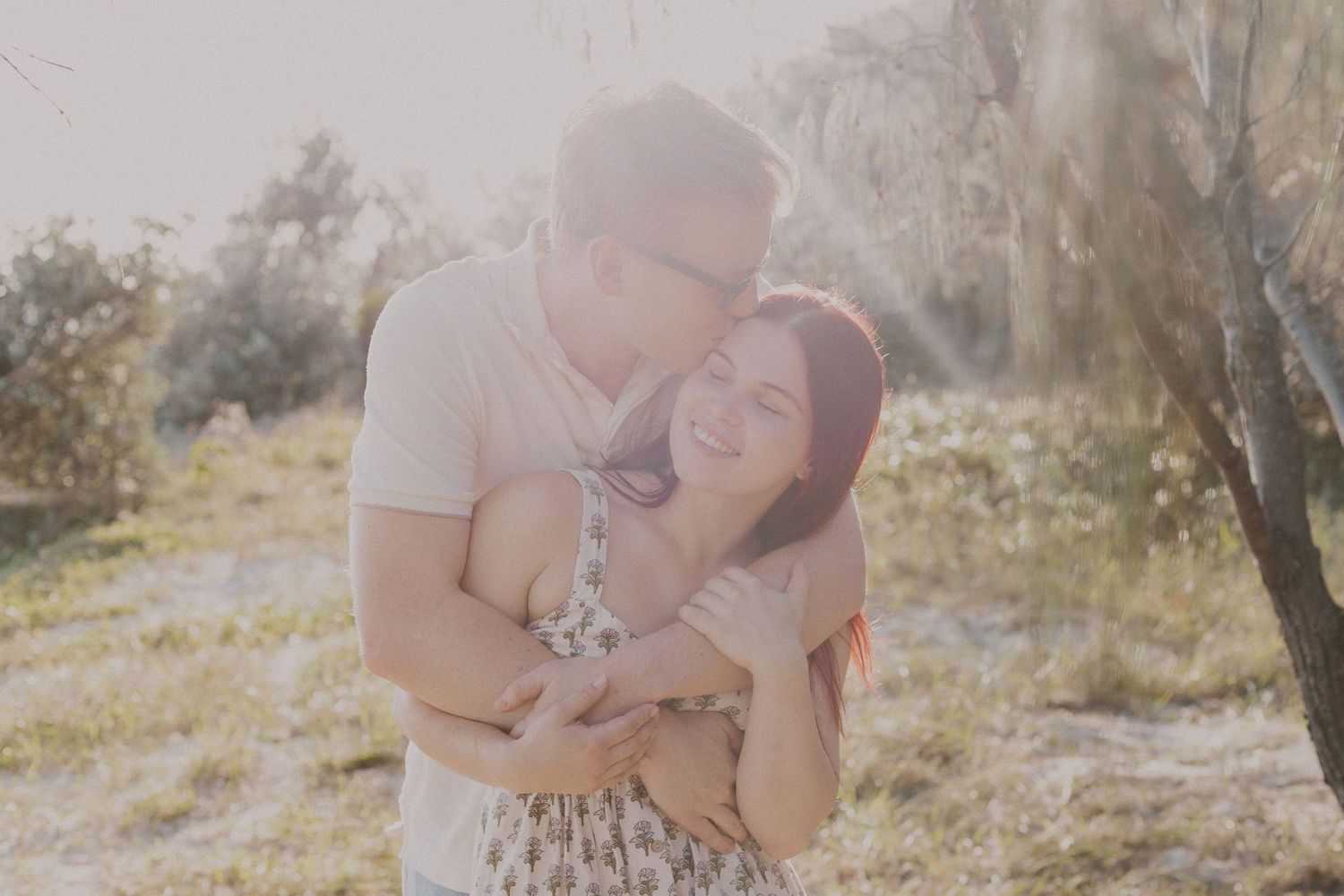 Couple embracing and laughing together in warm sunlit outdoor setting with soft natural light.