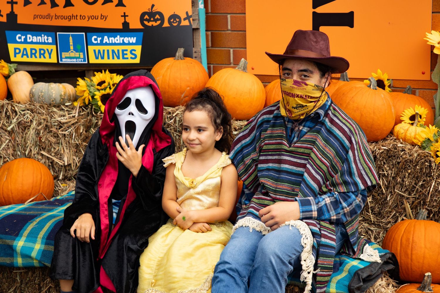 Three people in Halloween costumes pose with pumpkins at the Grange Pumpkin Patch event.