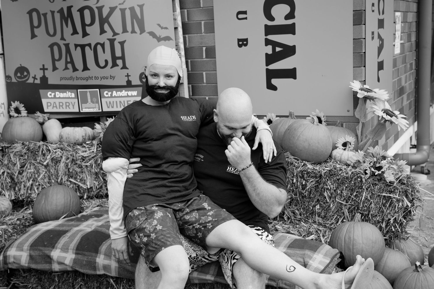 Two bald men sitting together on hay bales at Grange Pumpkin Patch in black and white photo.