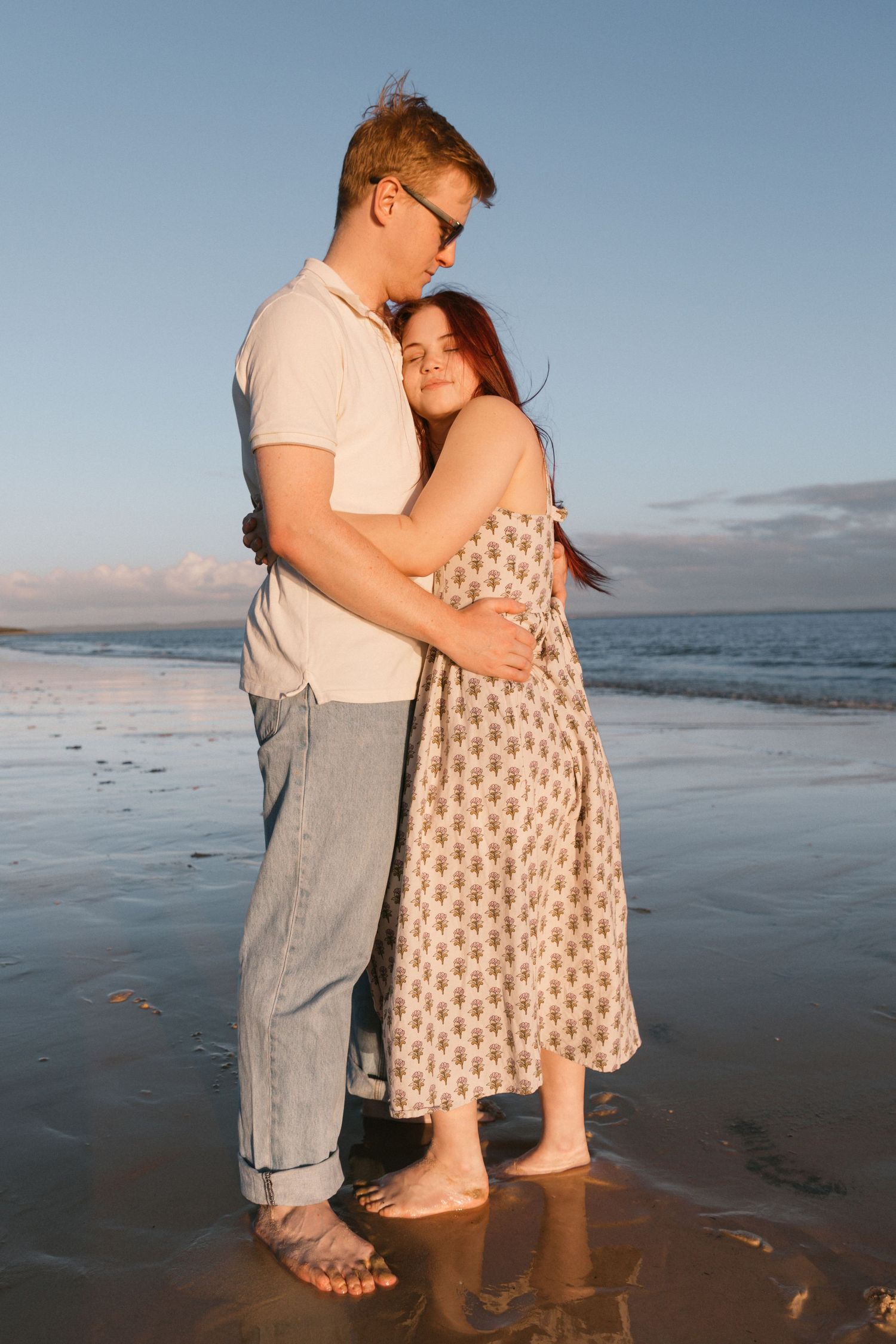 A couple embraces tenderly on a wet beach during a beautiful golden sunset.