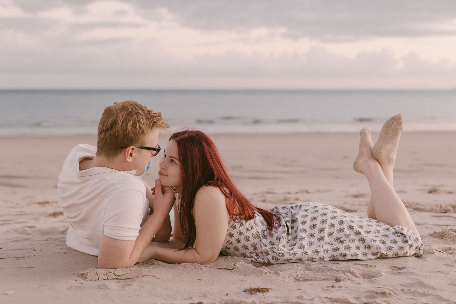 Romantic couple lying on sandy beach face to face at sunset in a tender moment.