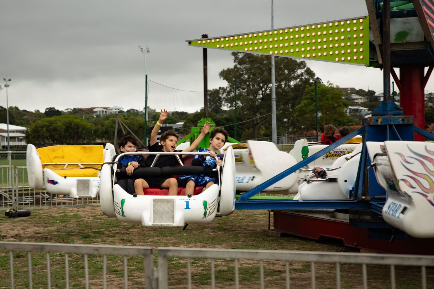 Excited children riding a spinning carnival ride at an outdoor fairground on a cloudy day.
