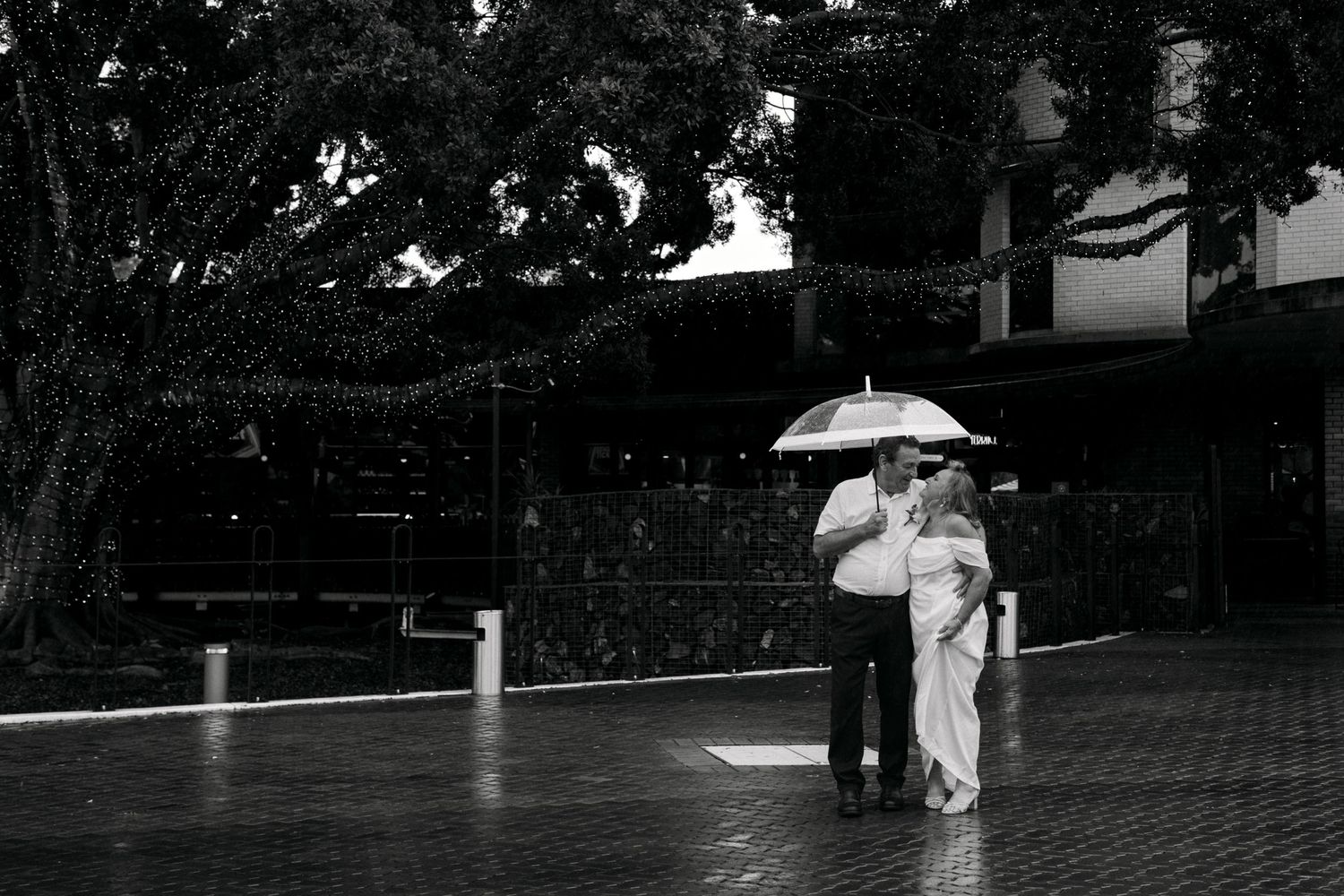 Bride and groom standing together under an umbrella during a rainy wedding shoot.