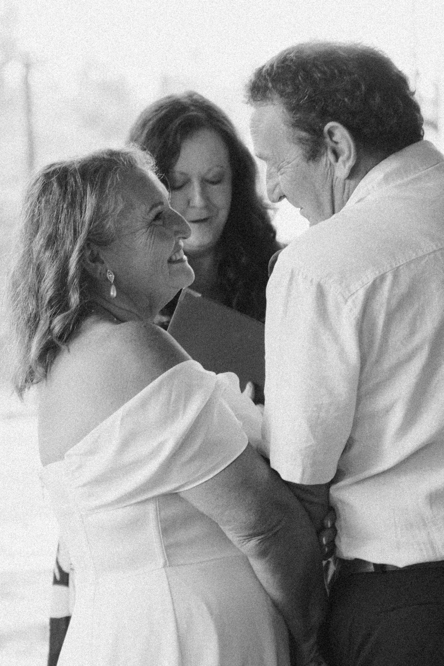 Bride and groom sharing a joyful moment with officiant during intimate wedding ceremony in black and white.